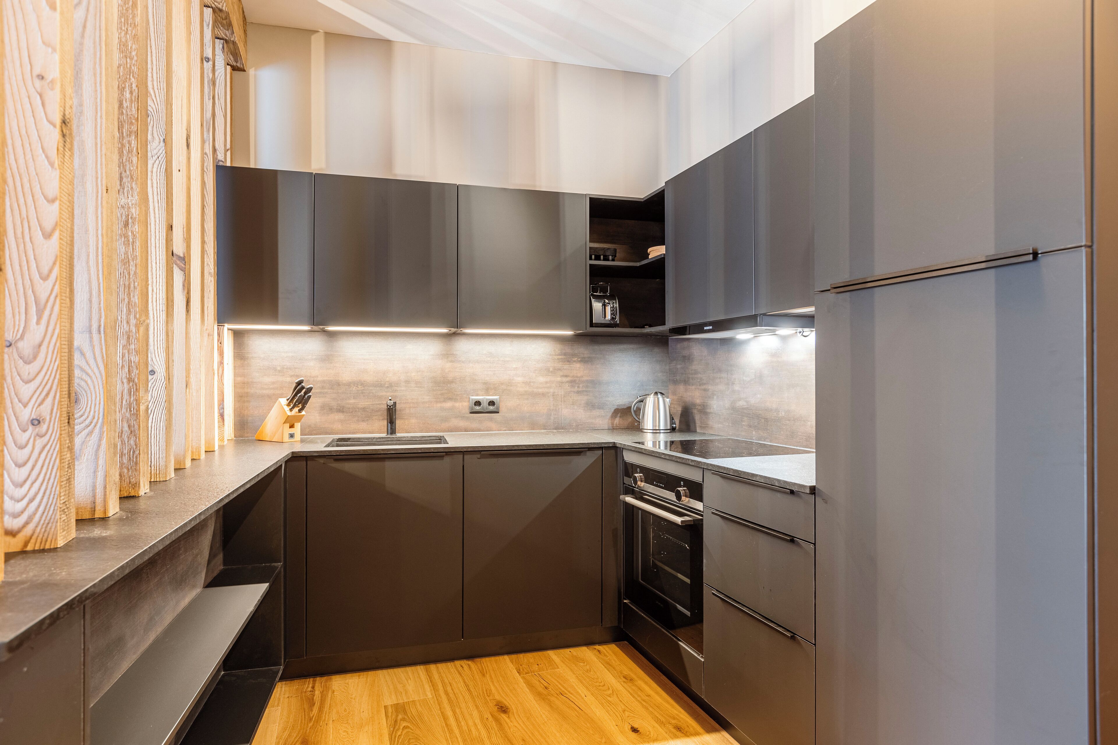 A modern kitchen with dark cabinetry, a wooden countertop, and a built-in oven.
