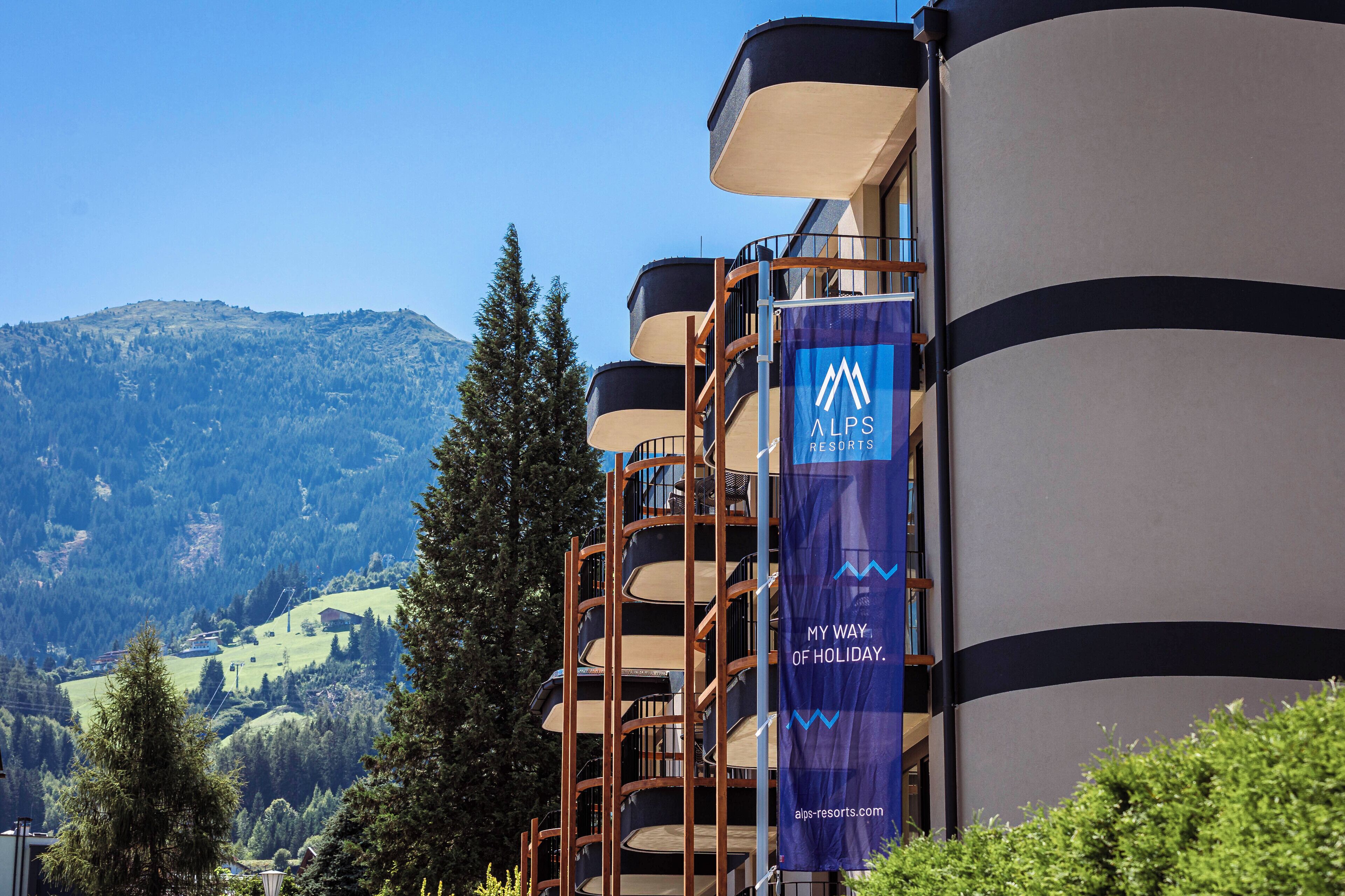 A building with a blue banner reading "Alps Resorts" and "My Way of Holiday."