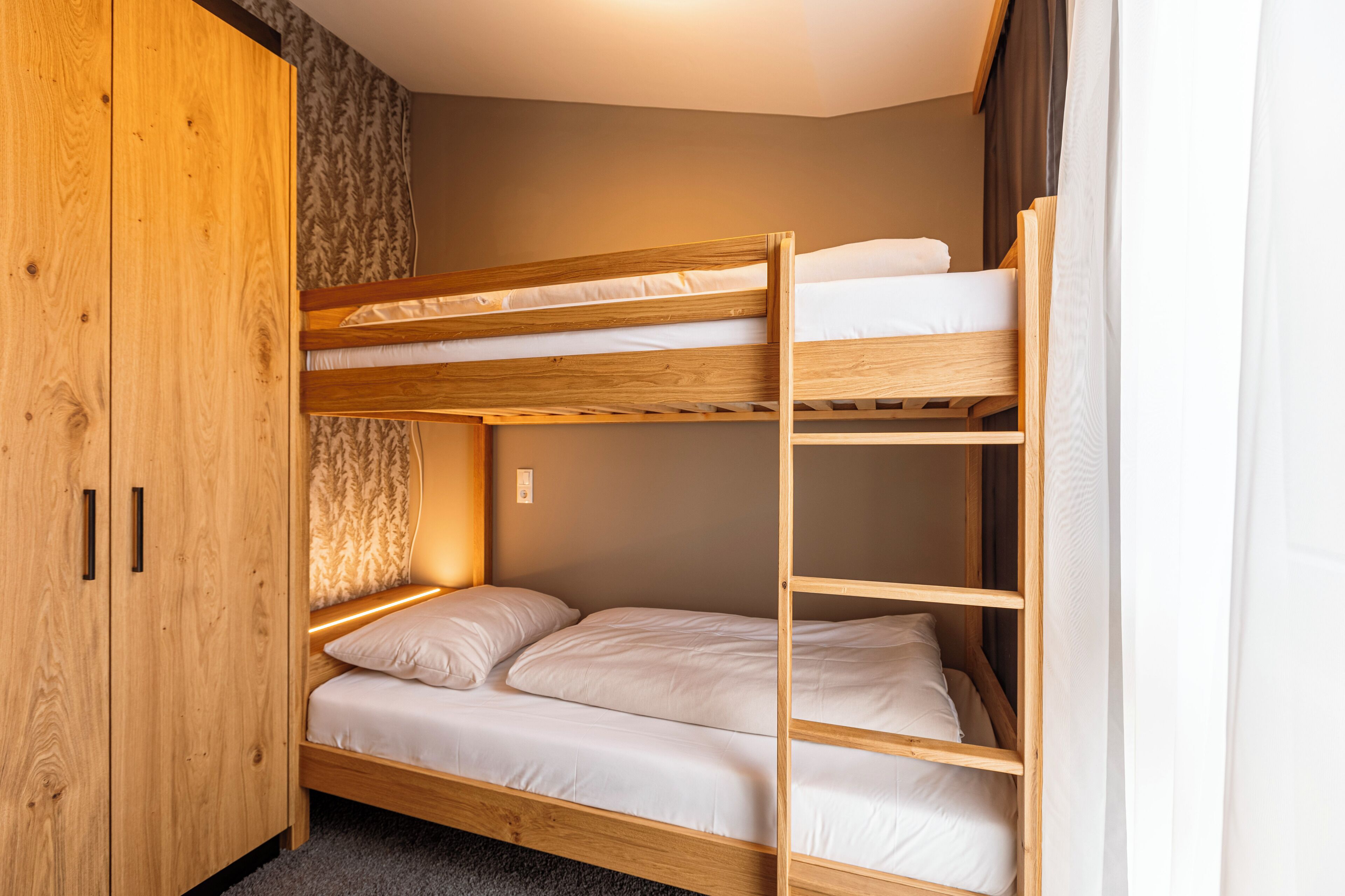 Une chambre avec un lit superposé, une armoire en bois et un mur décoré de motifs.