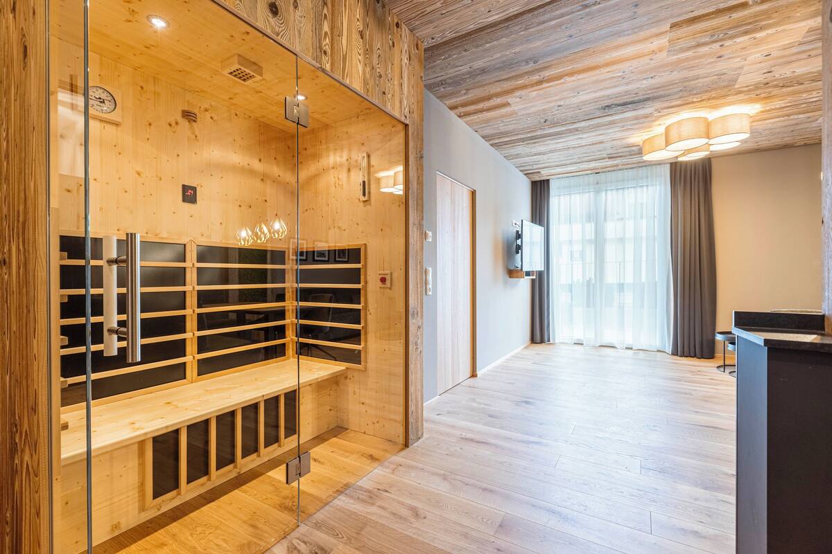 Una habitación de hotel moderna con paneles de madera, una sauna con paredes de cristal, un banco y un televisor.