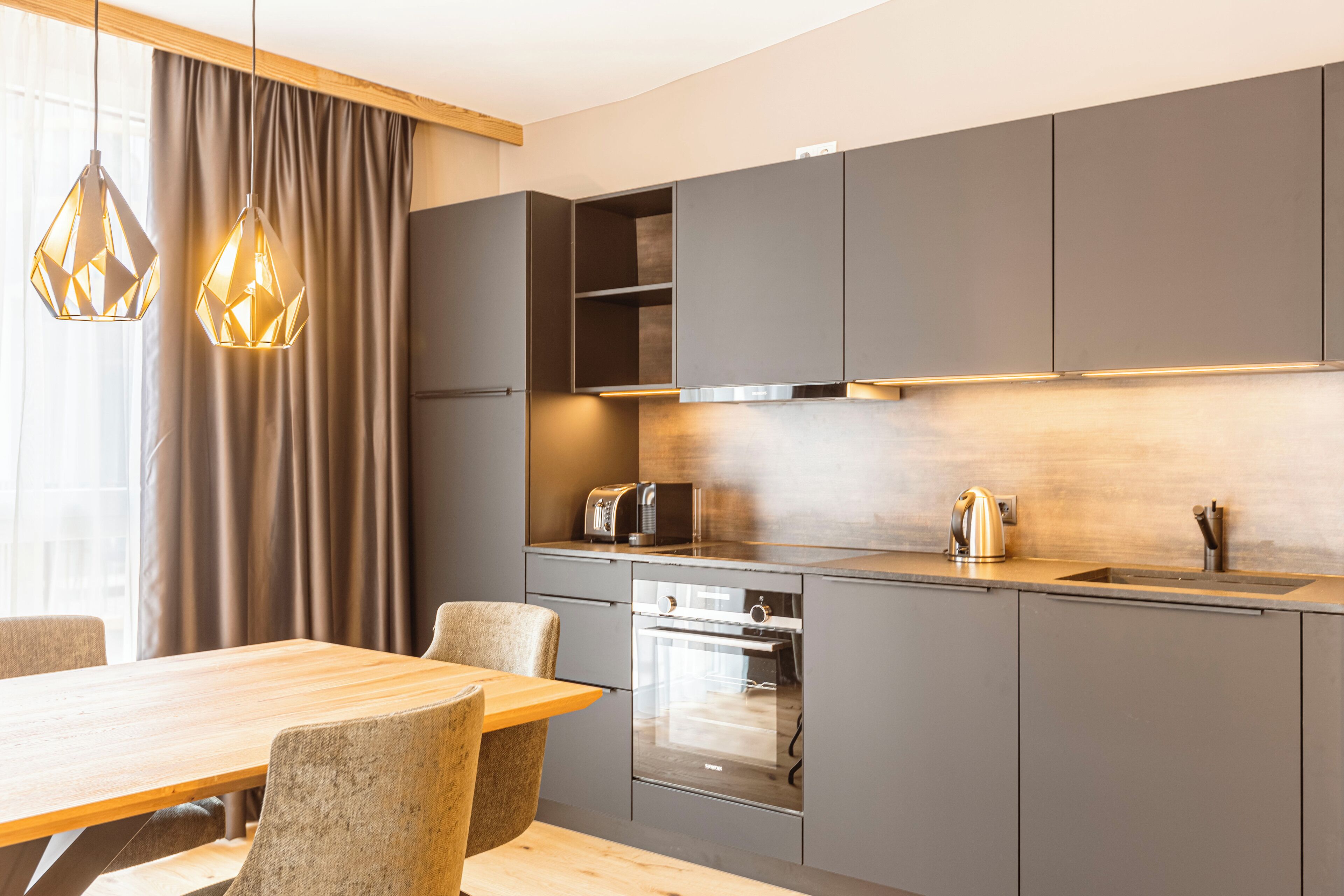 A modern kitchen with a wooden dining table, grey cabinets, and pendant lights.