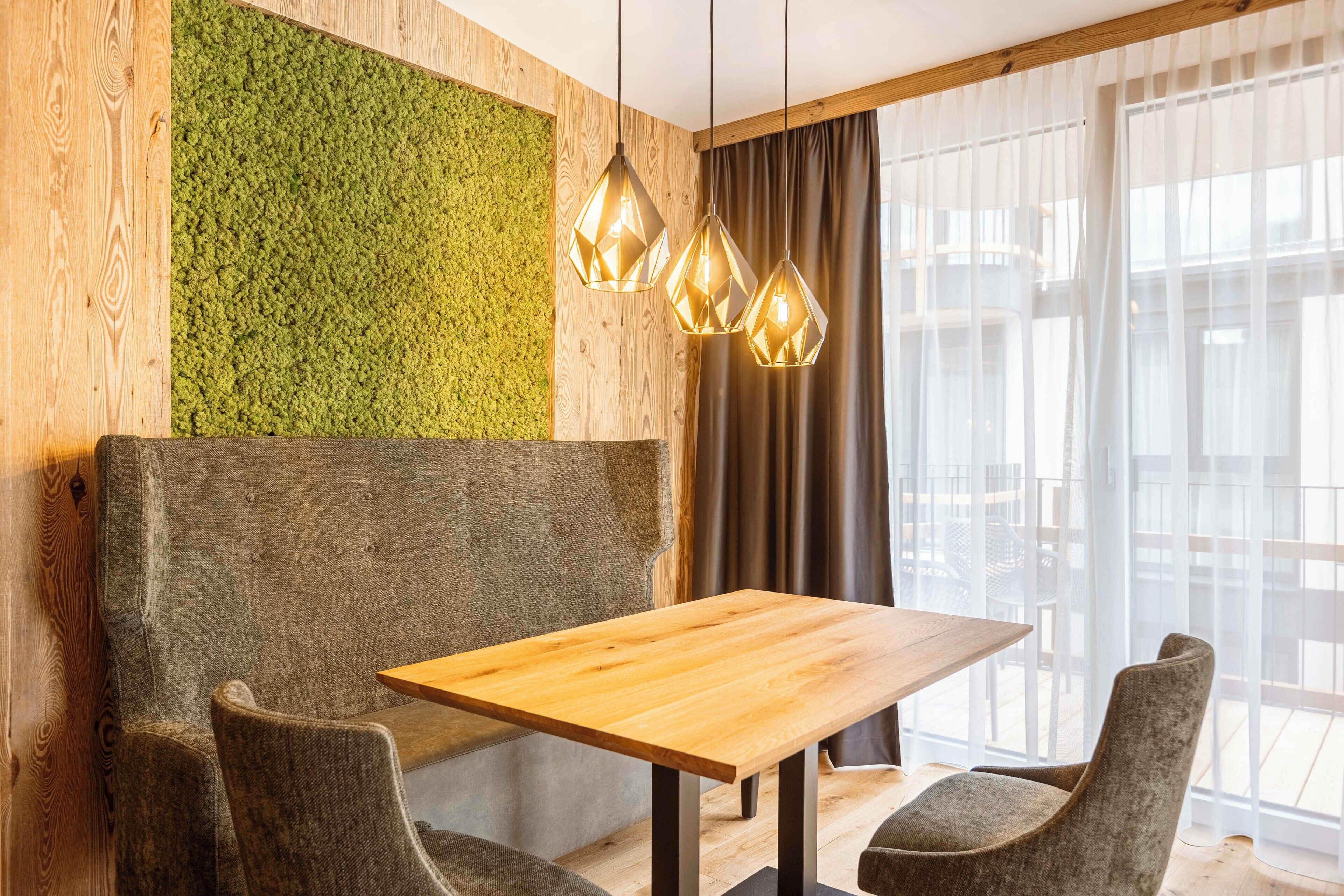 A cozy seating area with a wooden table and chairs, a green wall, and a large window with curtains.