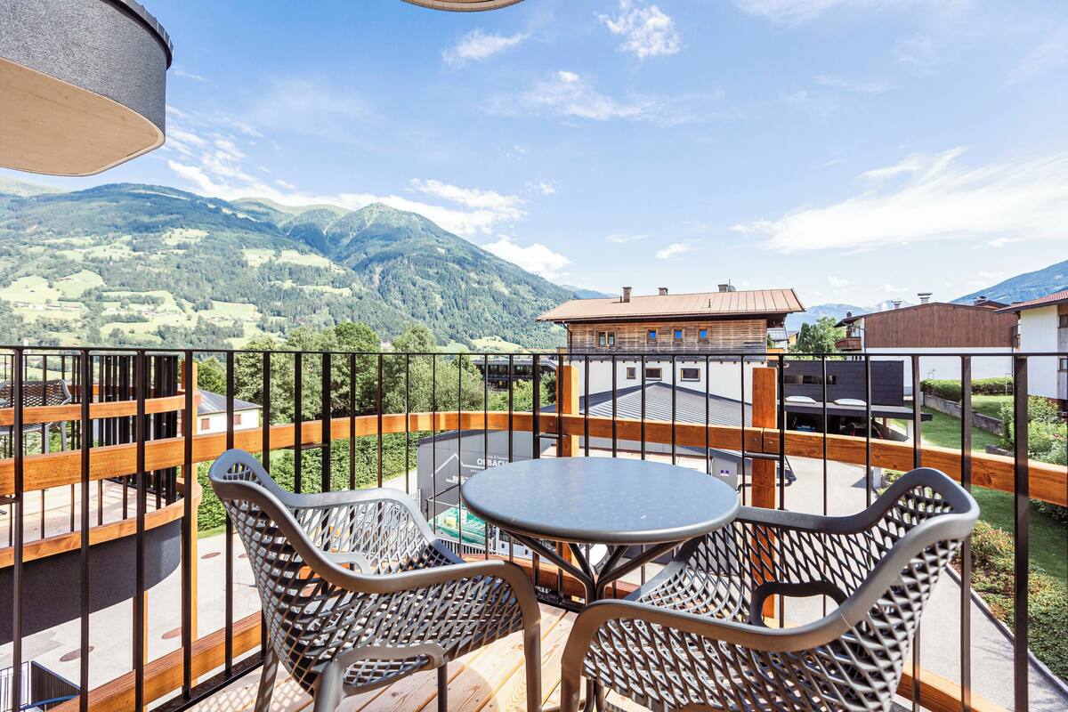 Un balcón con sillones de mimbre y una mesa, con vistas a un paisaje montañoso.