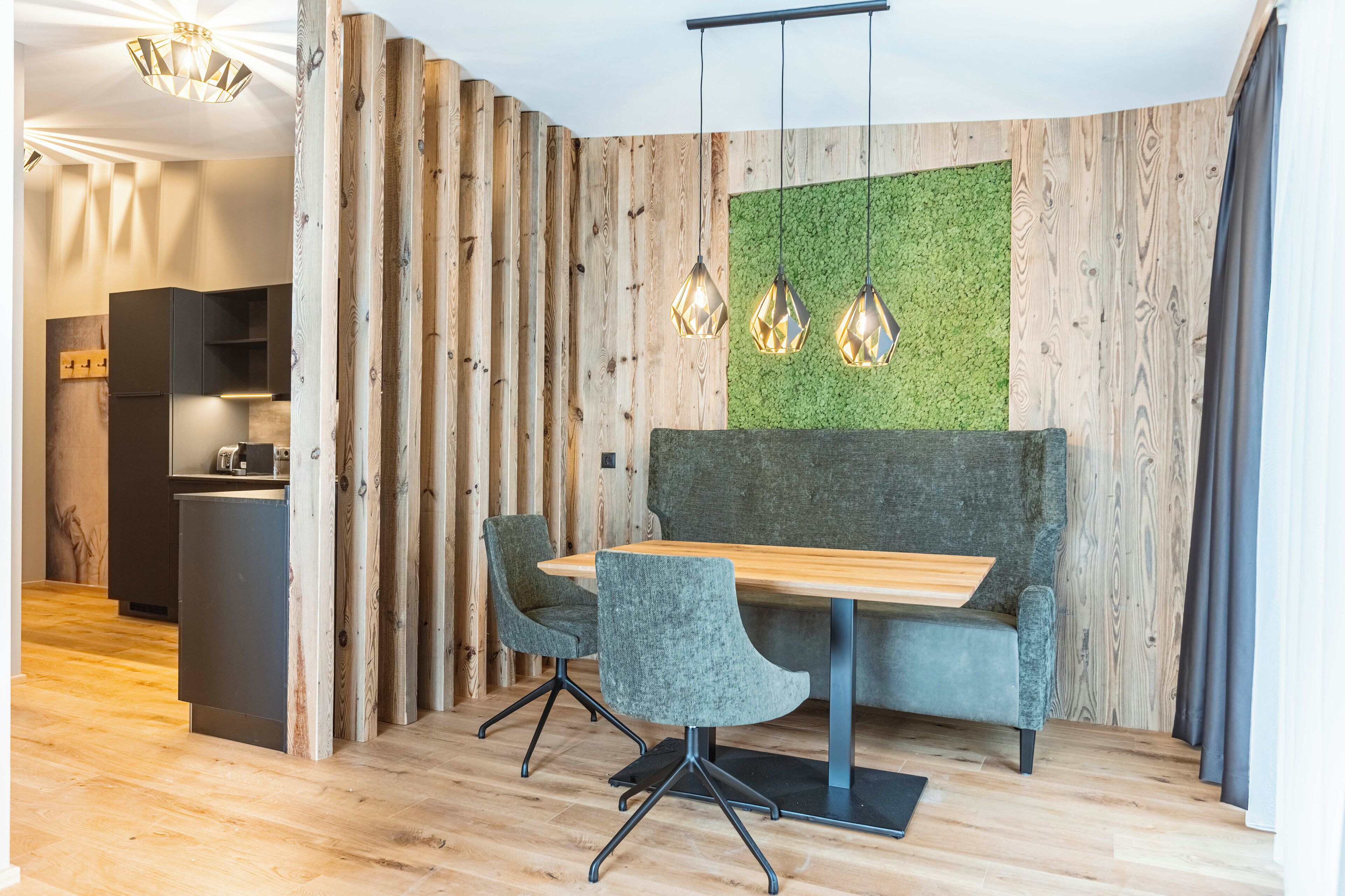A modern dining area with a wooden table, two upholstered chairs, and a green wall.