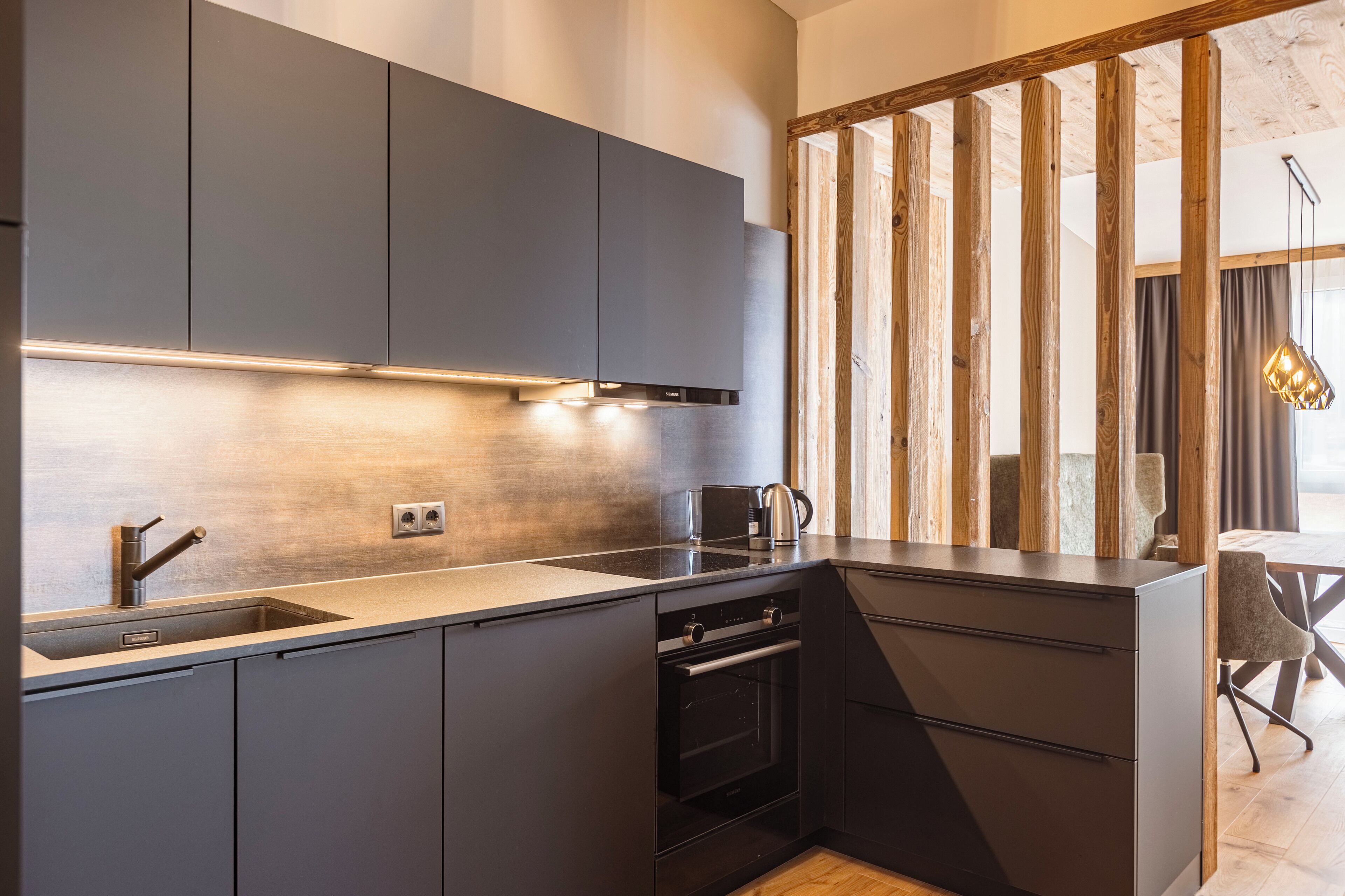A modern kitchen with dark cabinetry, a built-in oven, and a stainless steel sink.
