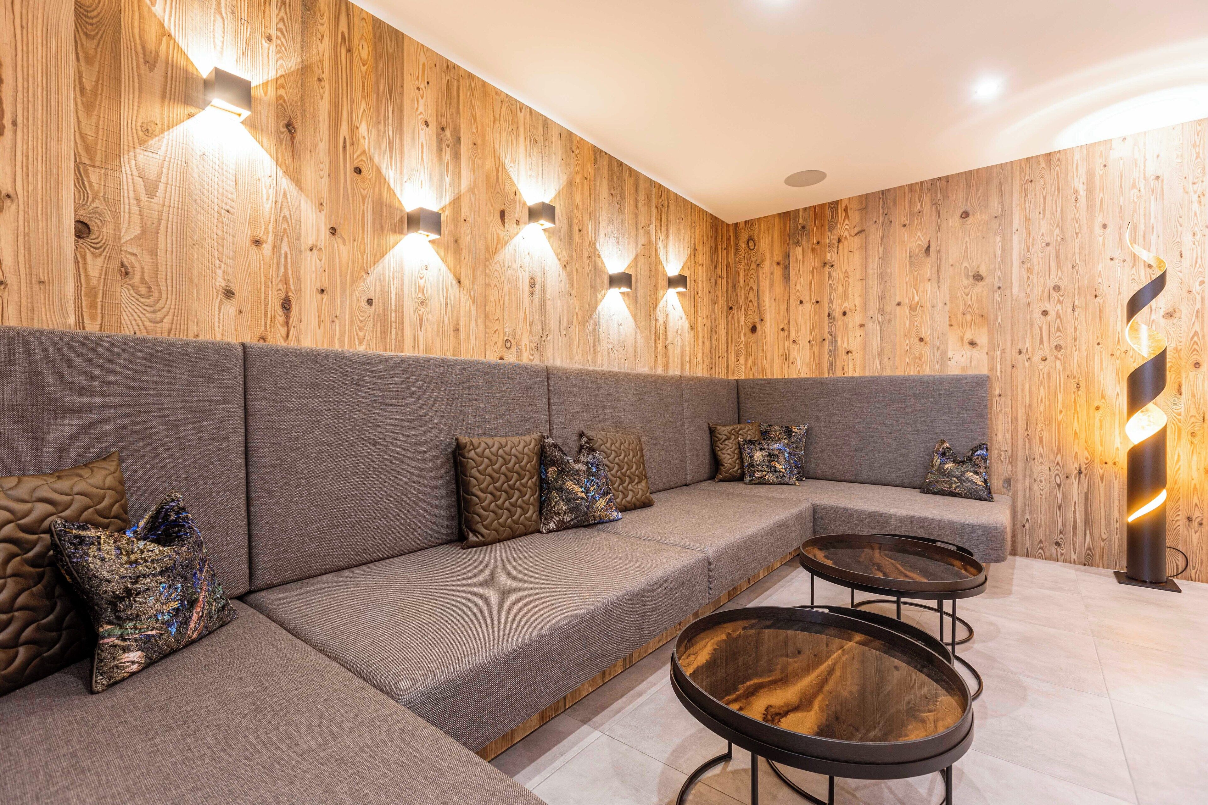 A modern lounge area with a wooden wall, grey upholstered seating, and a glass coffee table.