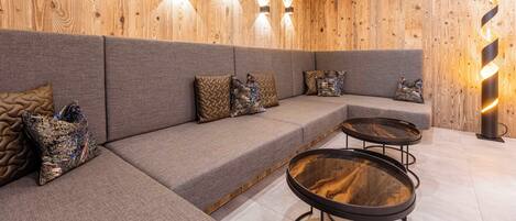 A modern lounge area with a wooden wall, grey upholstered seating, and a glass coffee table.