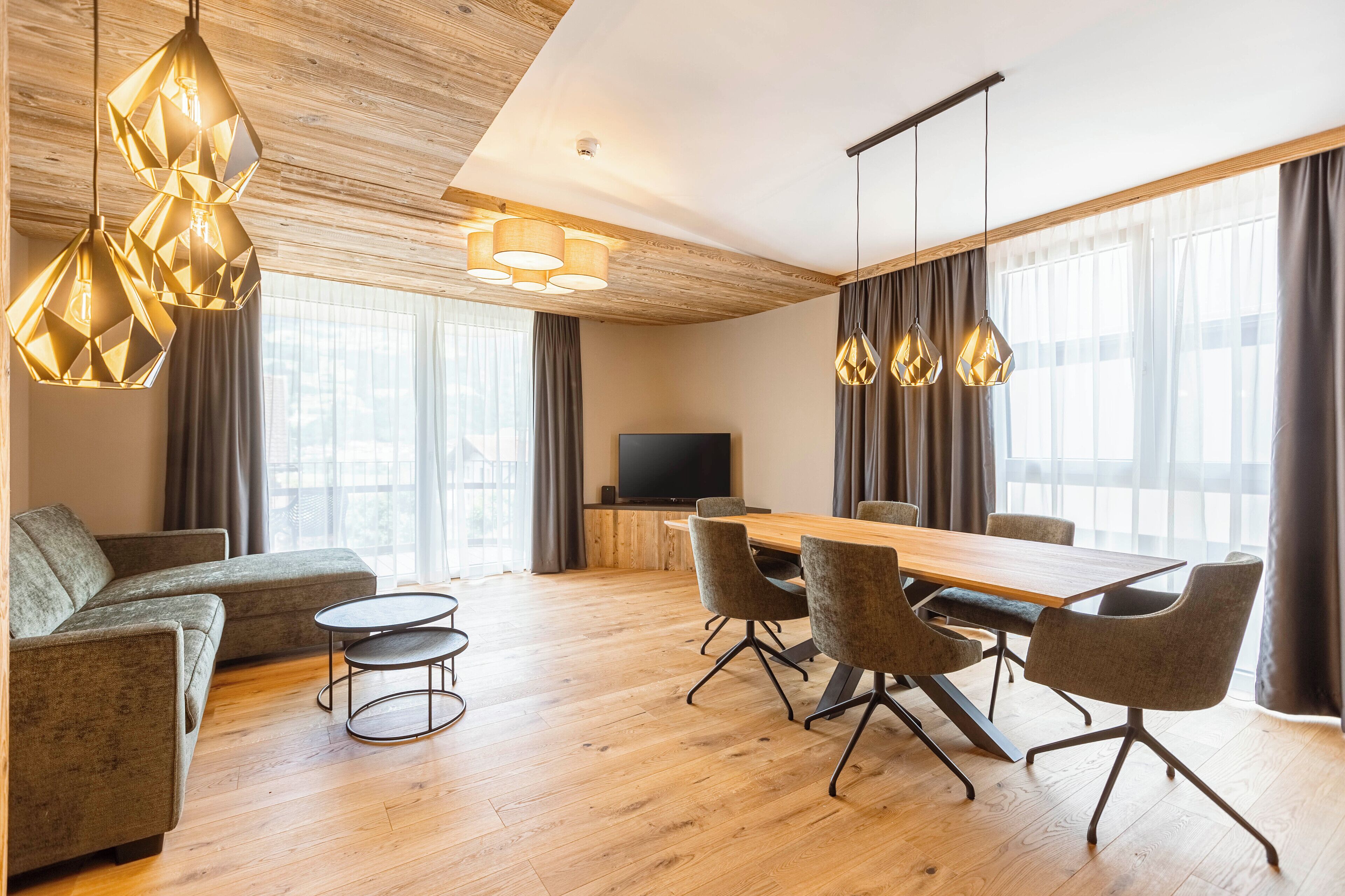 A modern living room with a wooden ceiling, a large dining table with chairs, a sofa, and a TV.