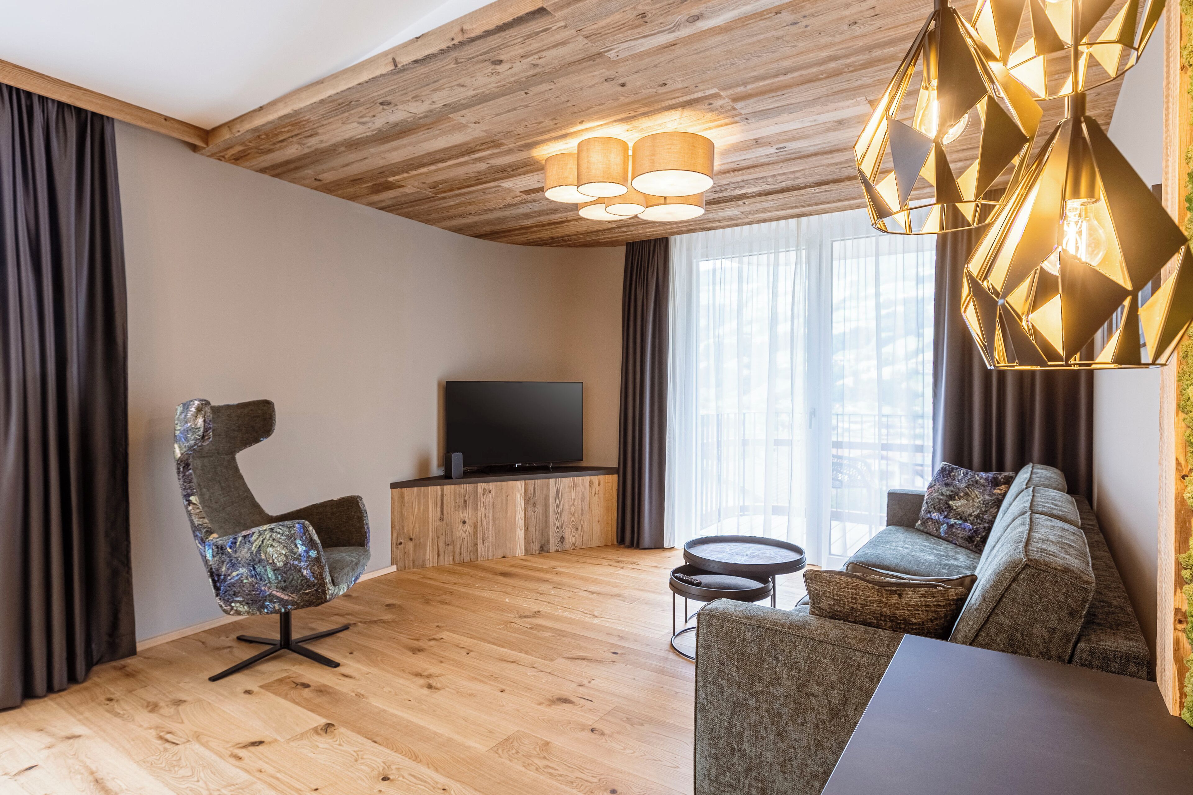 Ein modernes Wohnzimmer mit Holzboden, einem Flachbildfernseher, einer Couch, einem Sessel und einem kleinen runden Tisch.
