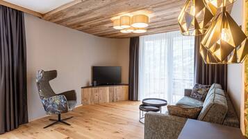 Ein modernes Wohnzimmer mit Holzboden, einem Flachbildfernseher, einer Couch, einem Sessel und einem kleinen runden Tisch.