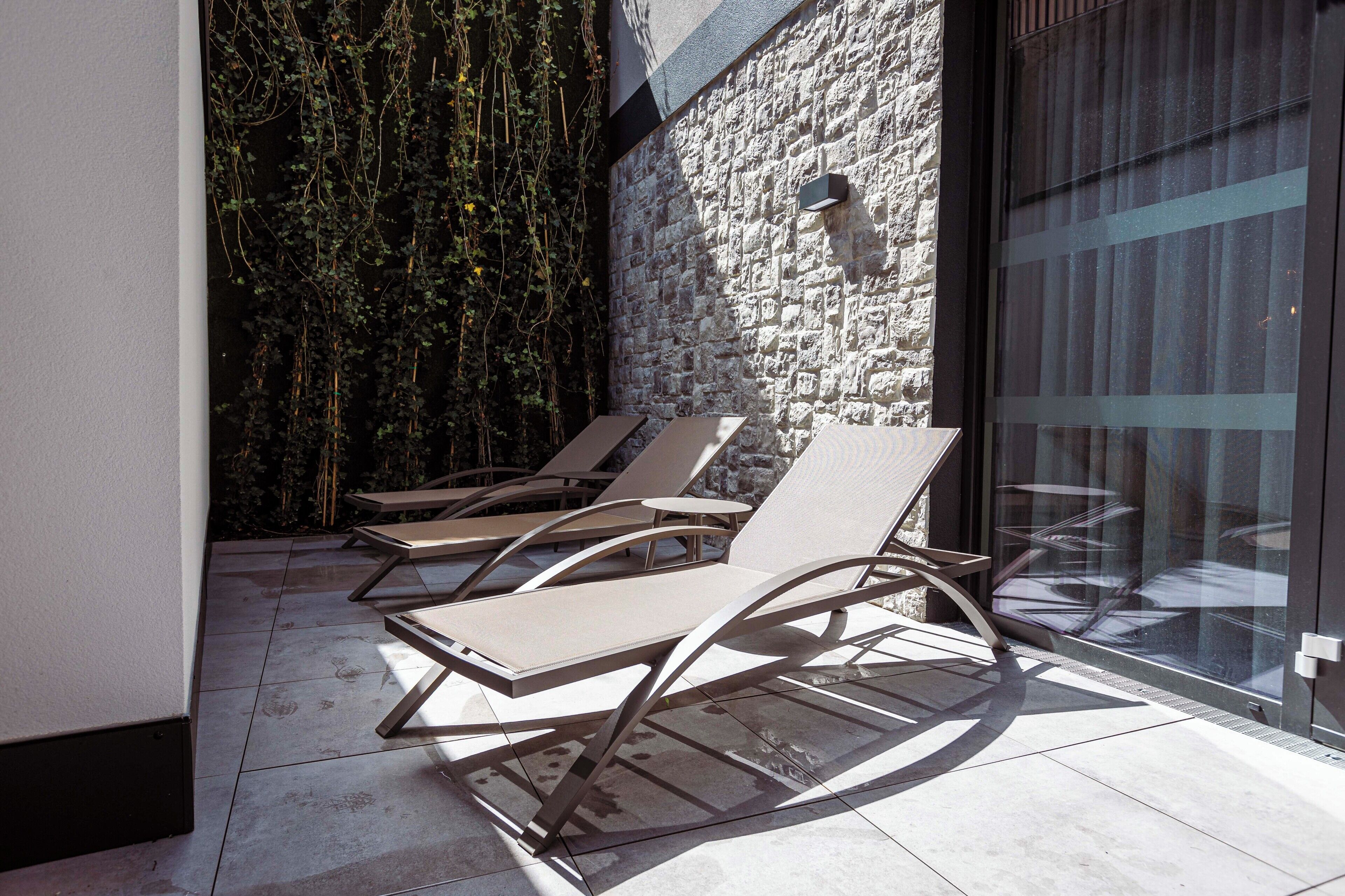 Un espacio exterior moderno con sillones de descanso y un muro de piedra de fondo.