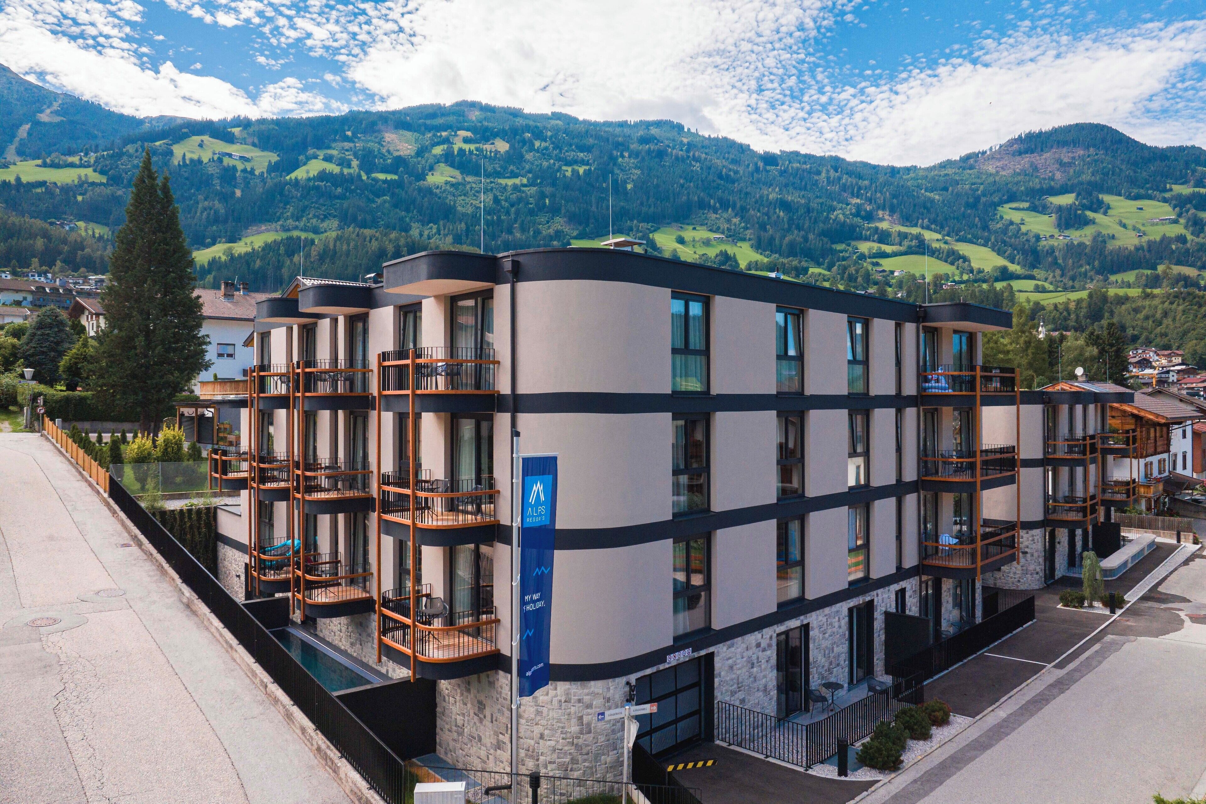 Ein mehrstöckiges Hotel mit Balkonen, einer Steinfassade und einer Bergkulisse.