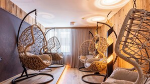 Une pièce avec quatre chaises suspendues, un plancher en bois, une grande fenêtre avec des rideaux et un mur en bois.