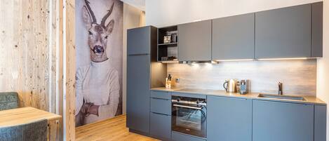 A modern kitchen with grey cabinets, a built-in oven, and a wooden floor.