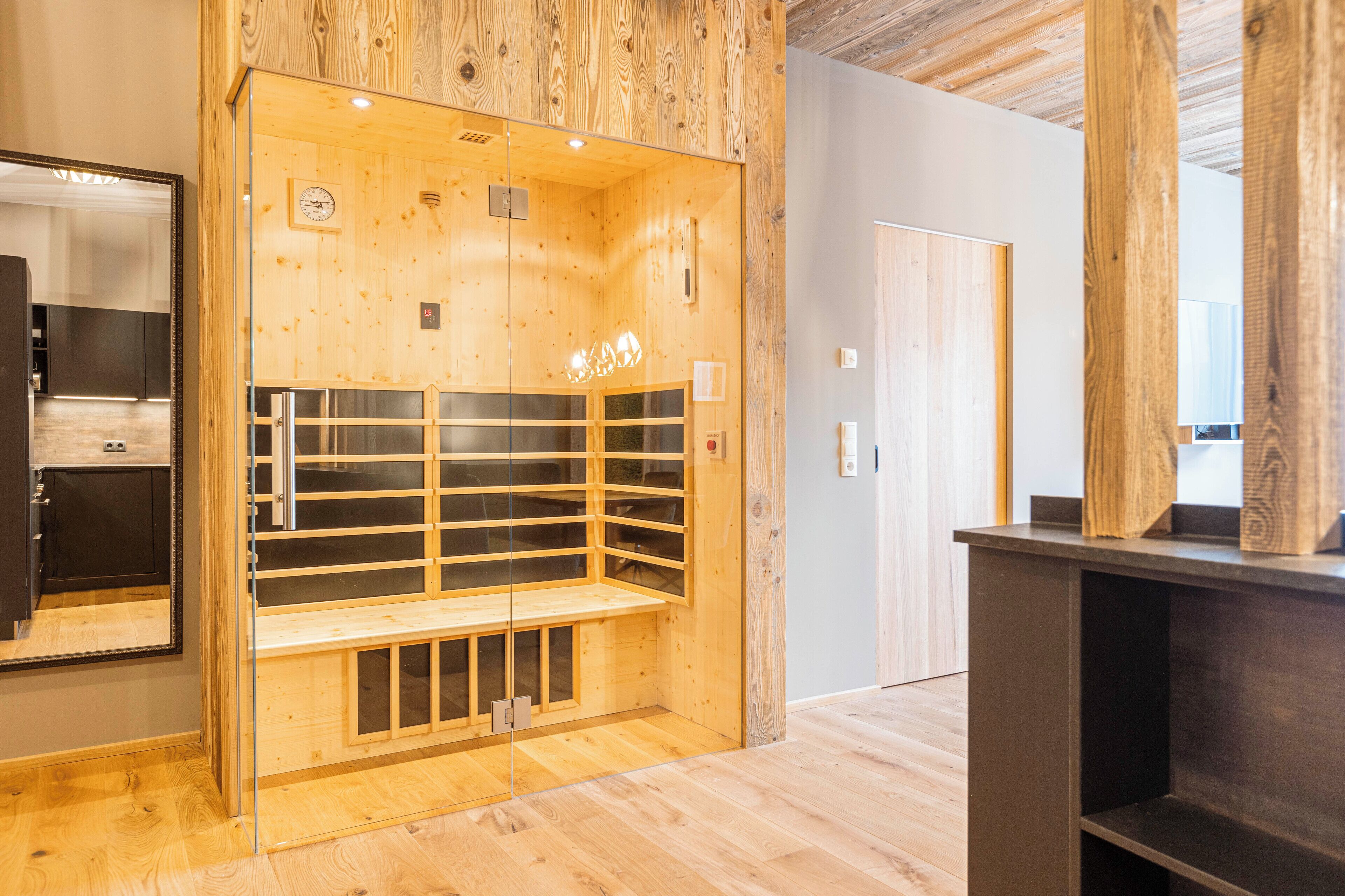 Un sauna en bois avec des panneaux de verre, un banc, une porte et un miroir sur le côté gauche.