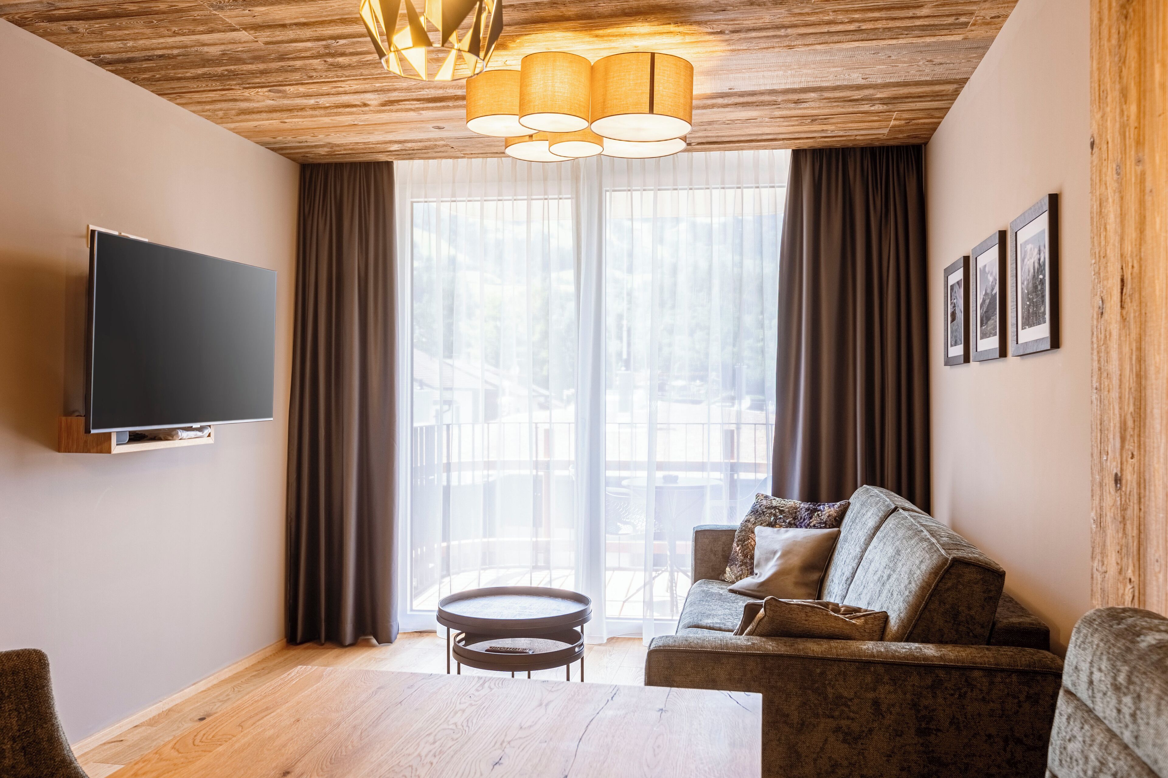 A modern living room with a flat-screen TV, a sofa, a coffee table, and a large window with curtains.