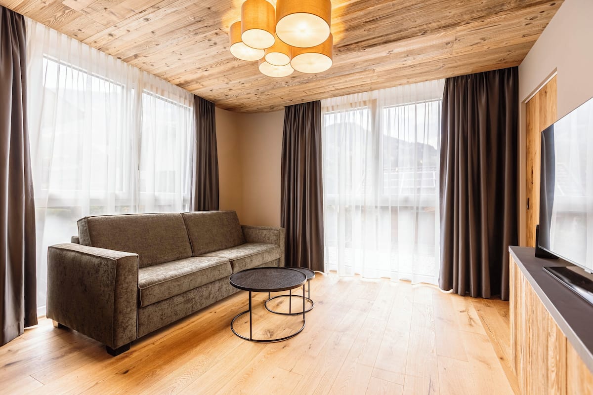 Una sala de estar moderna con techo de madera, un sofá, una mesa redonda de centro y un televisor sobre un mueble de madera.