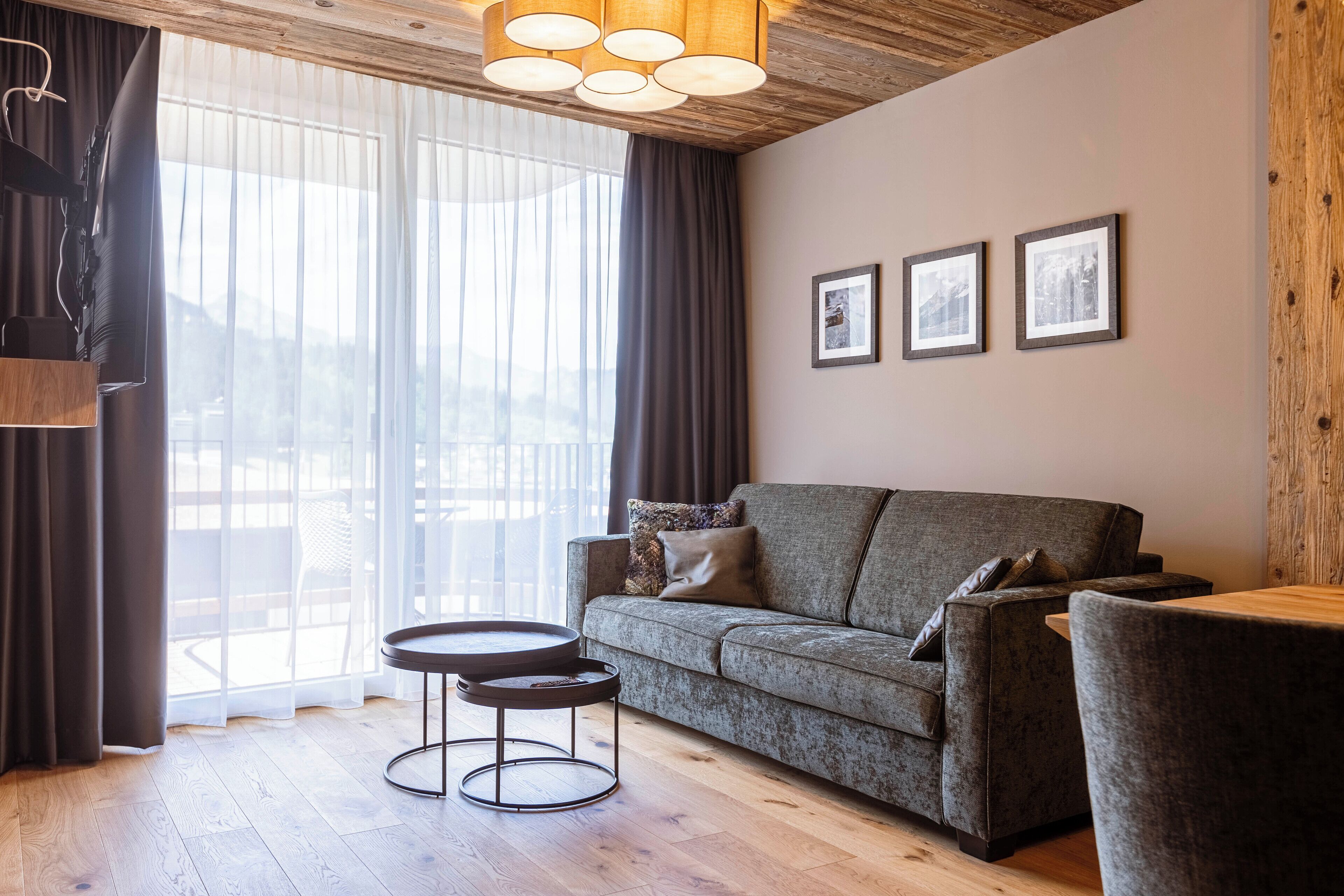 A modern living room with a grey sofa, a round coffee table, and a large window with sheer curtains.