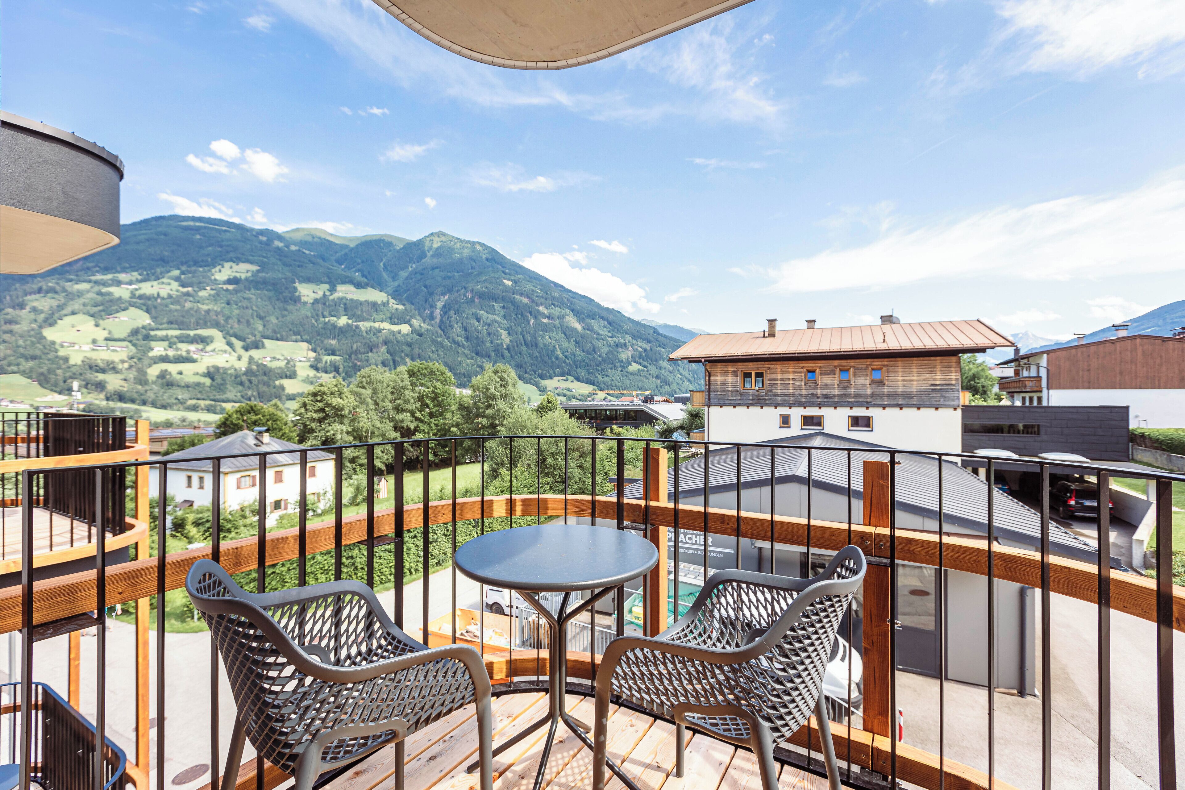 Ein Balkon mit Tisch und zwei Stühlen mit Blick auf eine gebirgige Landschaft.
