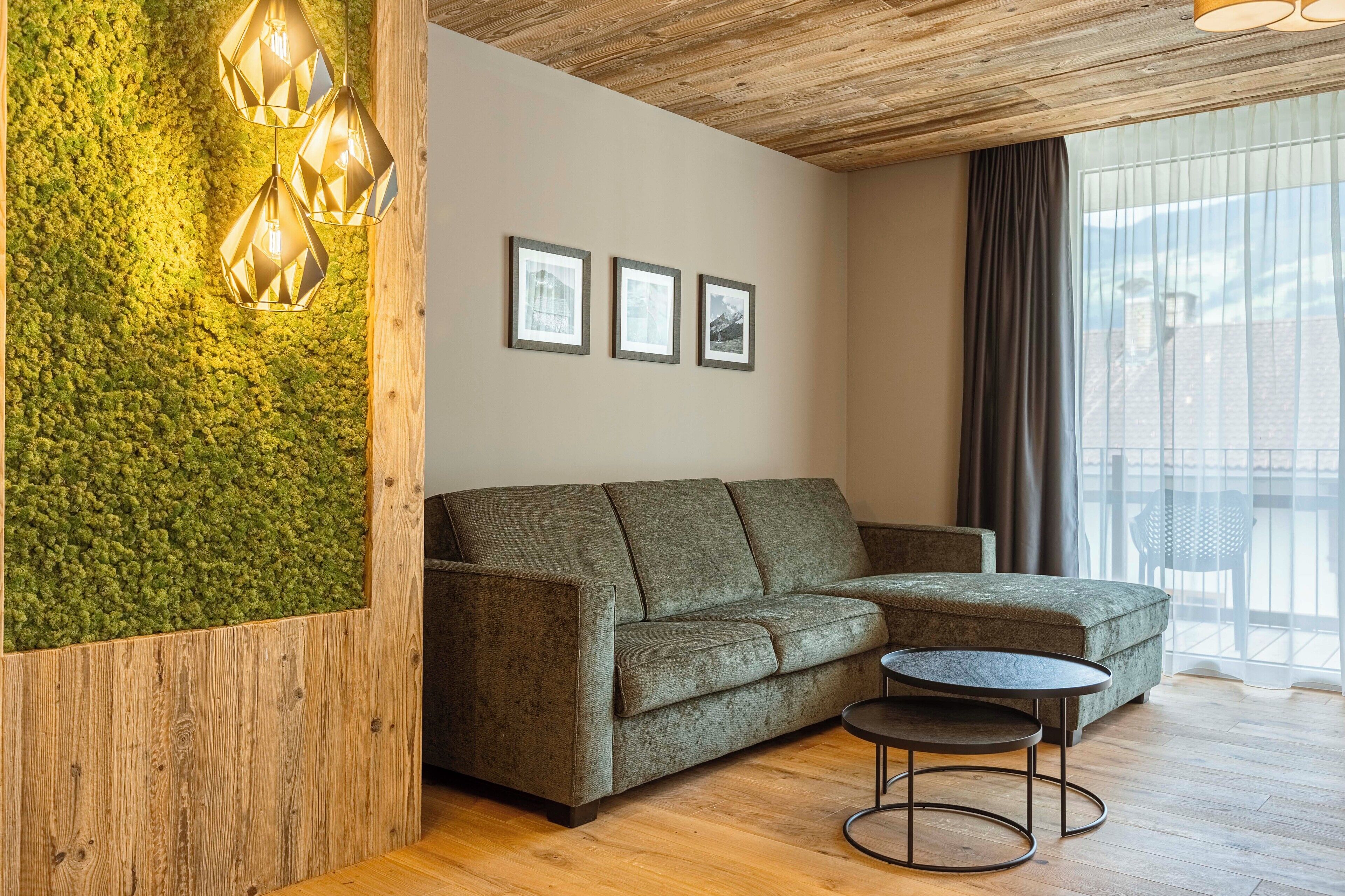 A modern living room with a green moss wall, a wooden ceiling, a grey sofa, and a round table.