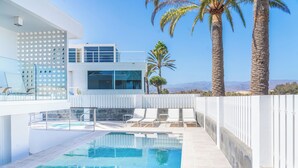 A modern pool area with a clear view of the pool, lounge chairs, and a white building with large windows.