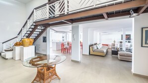 A spacious living area with a glass-top table, a sofa, and a staircase leading to an upper level.