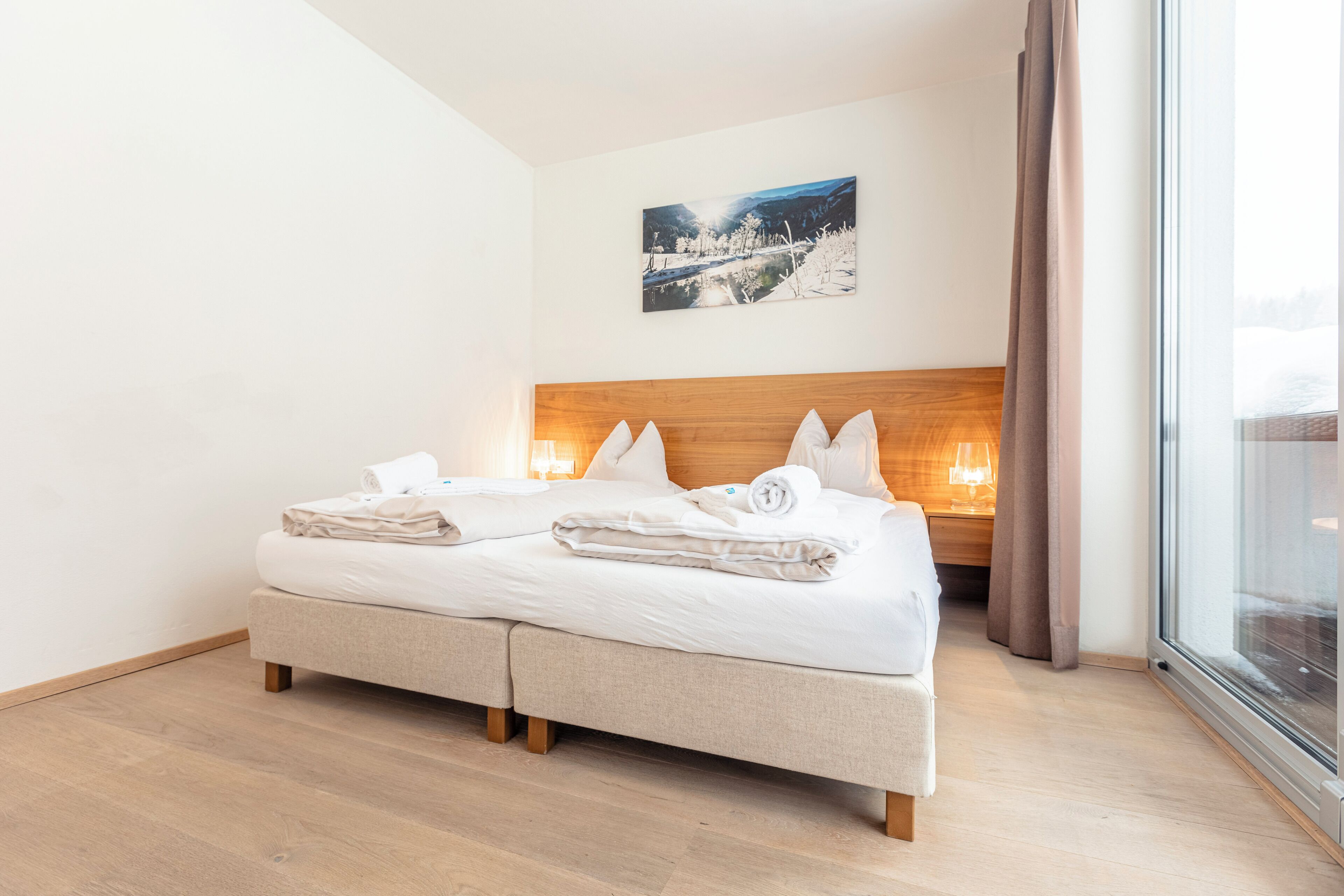 Une chambre d’hôtel moderne avec un lit double, une tête de lit en bois, une grande fenêtre donnant sur un beau paysage et un tableau au mur.