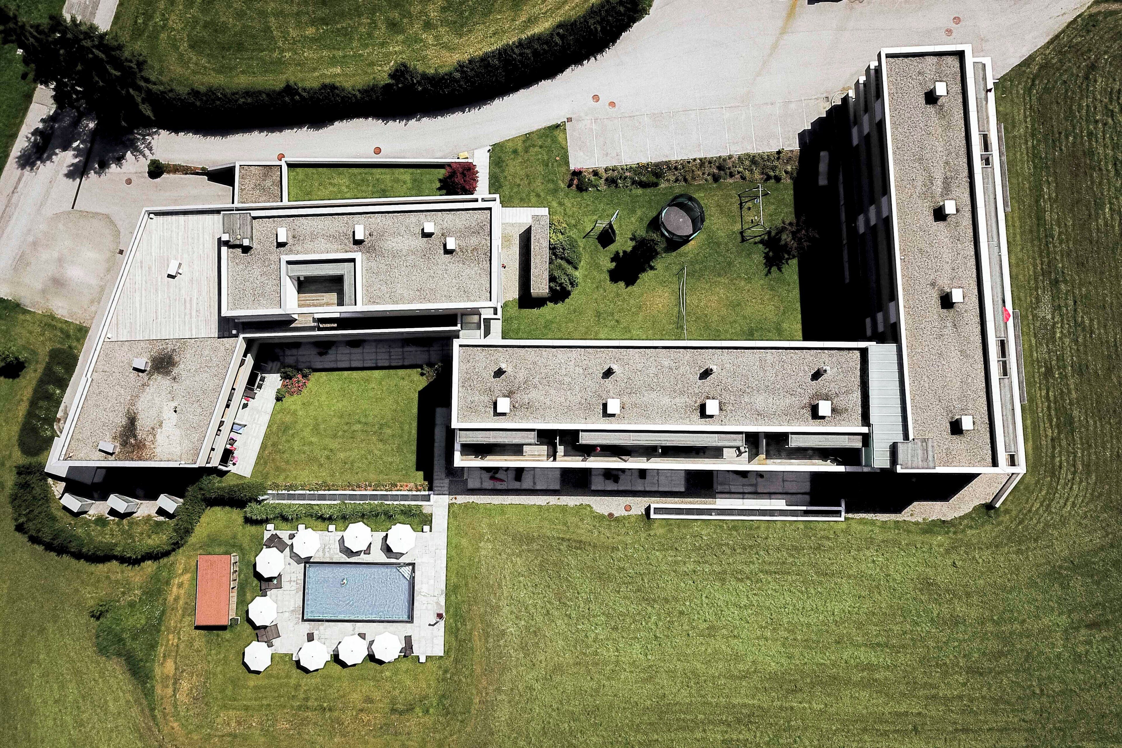 An aerial view of a modern building with a rooftop pool, outdoor seating, and a landscaped garden.
