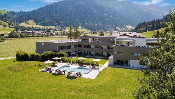 Un hotel moderno con piscina, mobiliario exterior y vistas a las montañas.