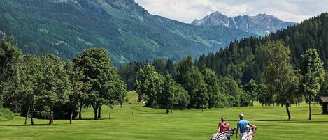 A golf course with a mountainous backdrop, trees, and a clear sky.