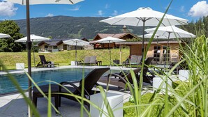 Zona junto a la piscina con sillones de descanso y sombrillas, con vistas a un paisaje montañoso.