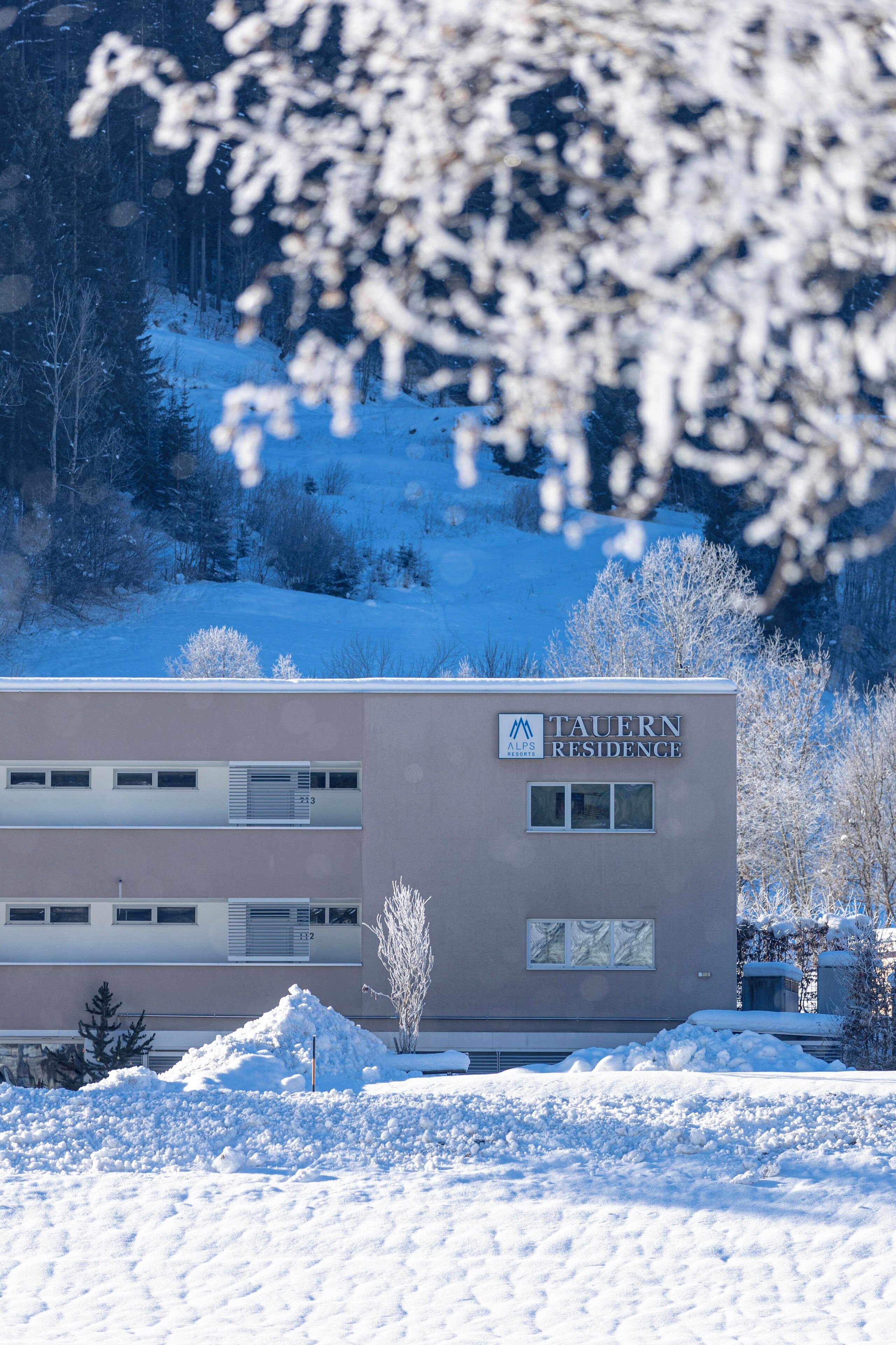 A building labeled "TAUERN RESIDENCE" with a snow-covered landscape and trees in the background.