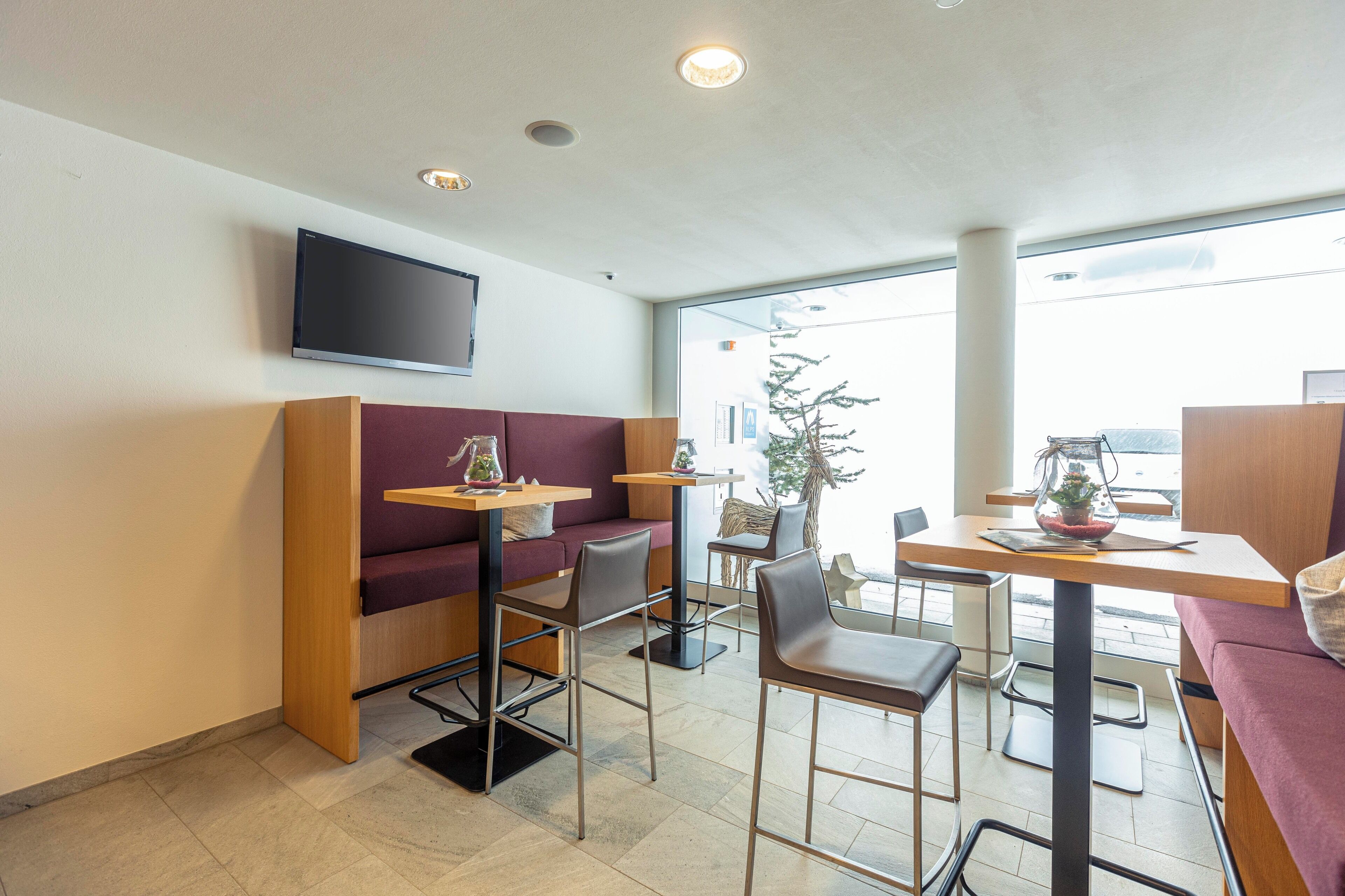 A modern cafe with a wooden bar, cushioned seating, and a flat-screen TV.