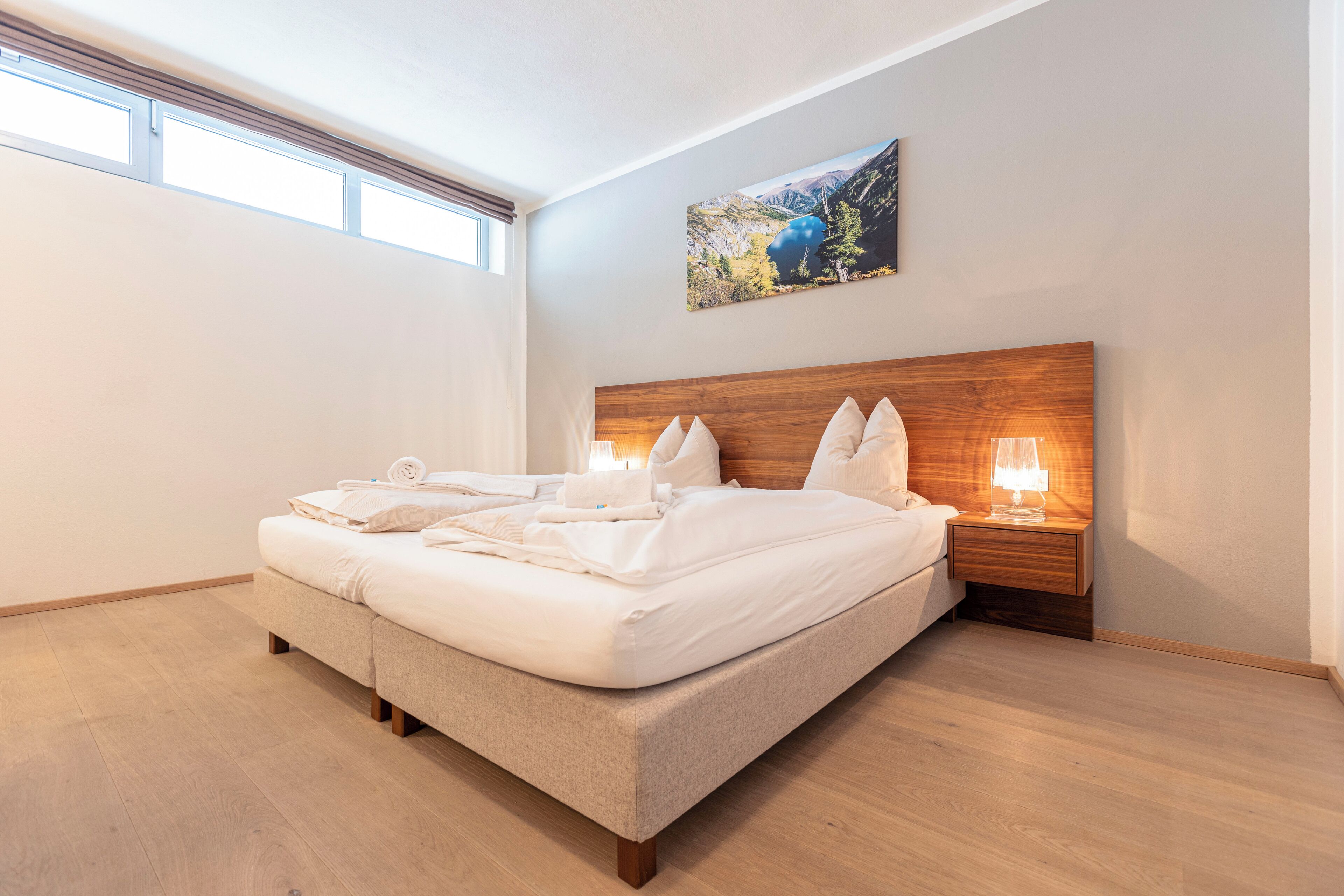 Una cama bien hecha, con almohadas y una colcha, un cabecero de madera, una mesita de noche con una lámpara y un cuadro en la pared.