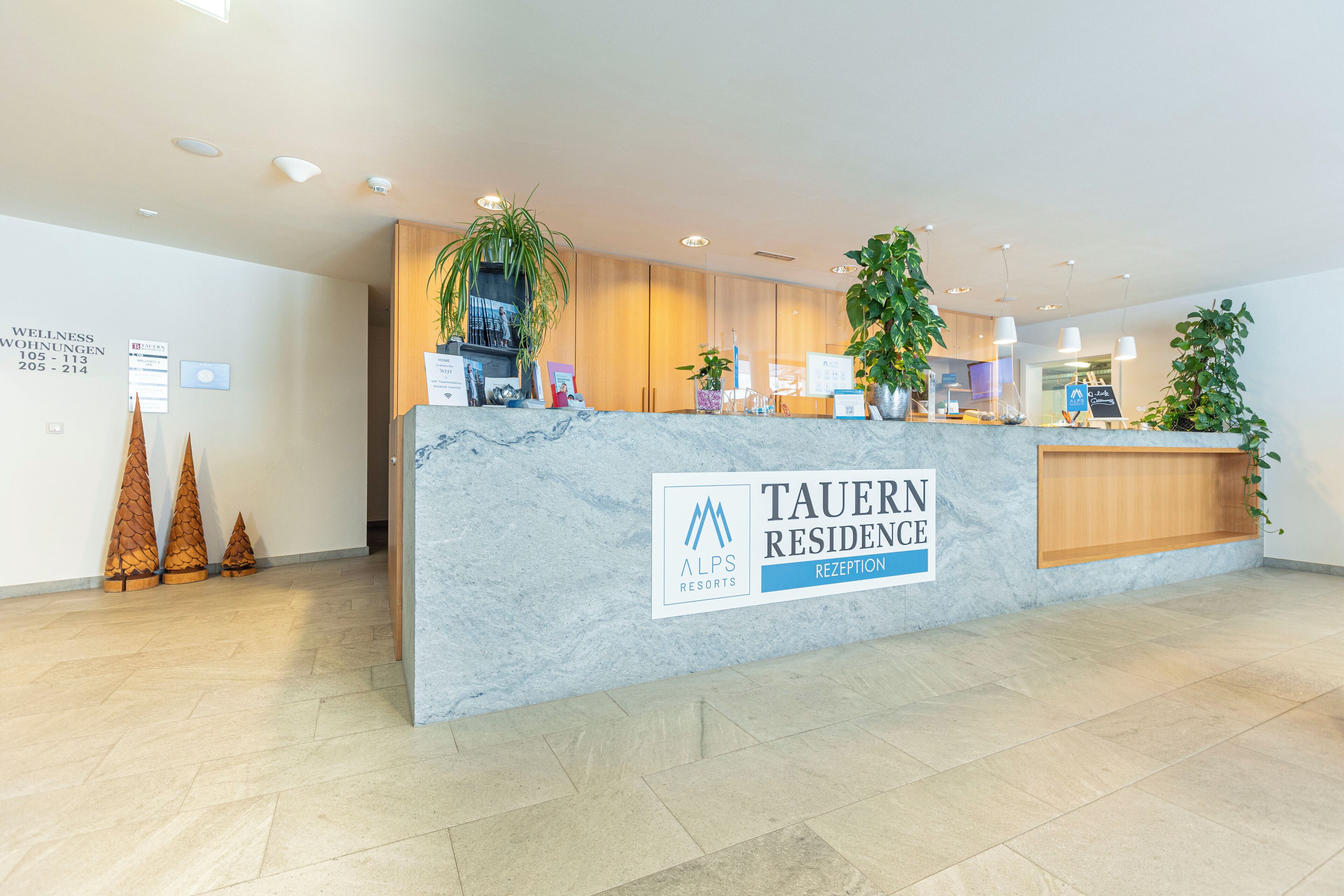A reception desk at Tauern Residence with a marble top, wooden paneling, and potted plants.