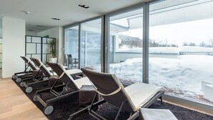 Un espacio interior moderno con amplios ventanales, un área de descanso con sillas y mesas, y vistas a un paisaje nevado.