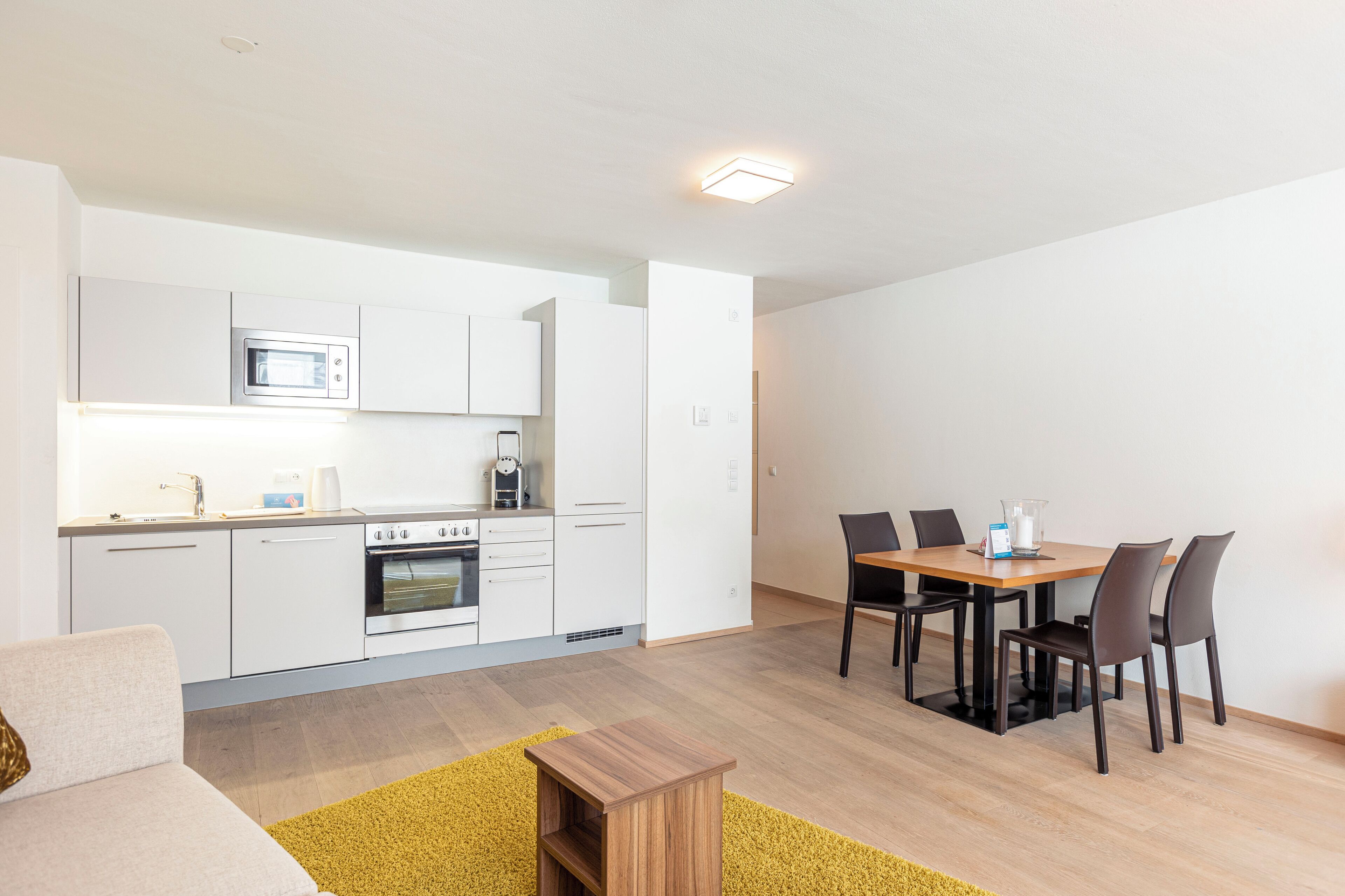 A modern kitchen with white cabinets, a microwave, and a stove. There is a dining area with a wooden table and four chairs.