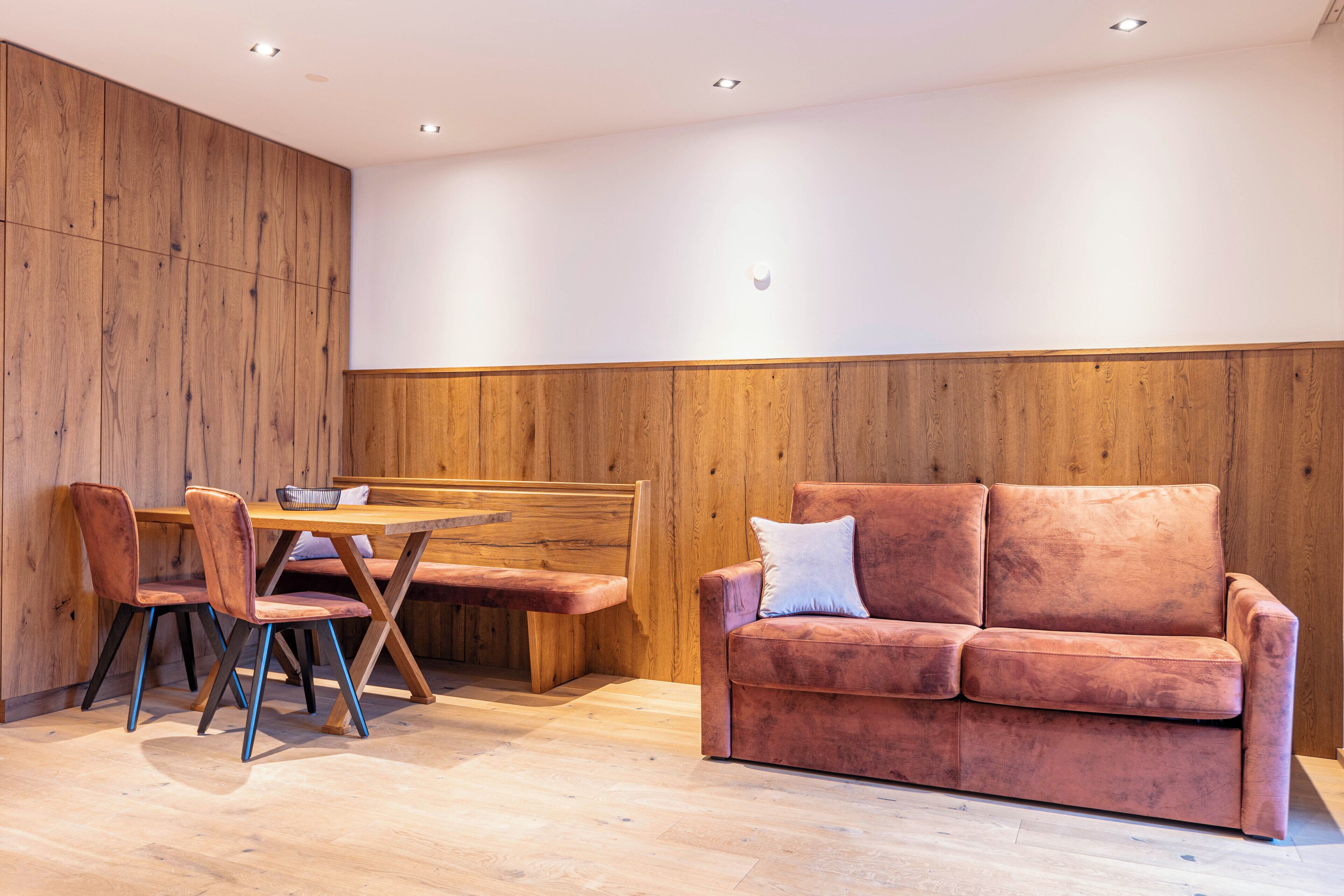 A modern interior with a wooden panel wall, a wooden dining table with chairs, and a plush red sofa.