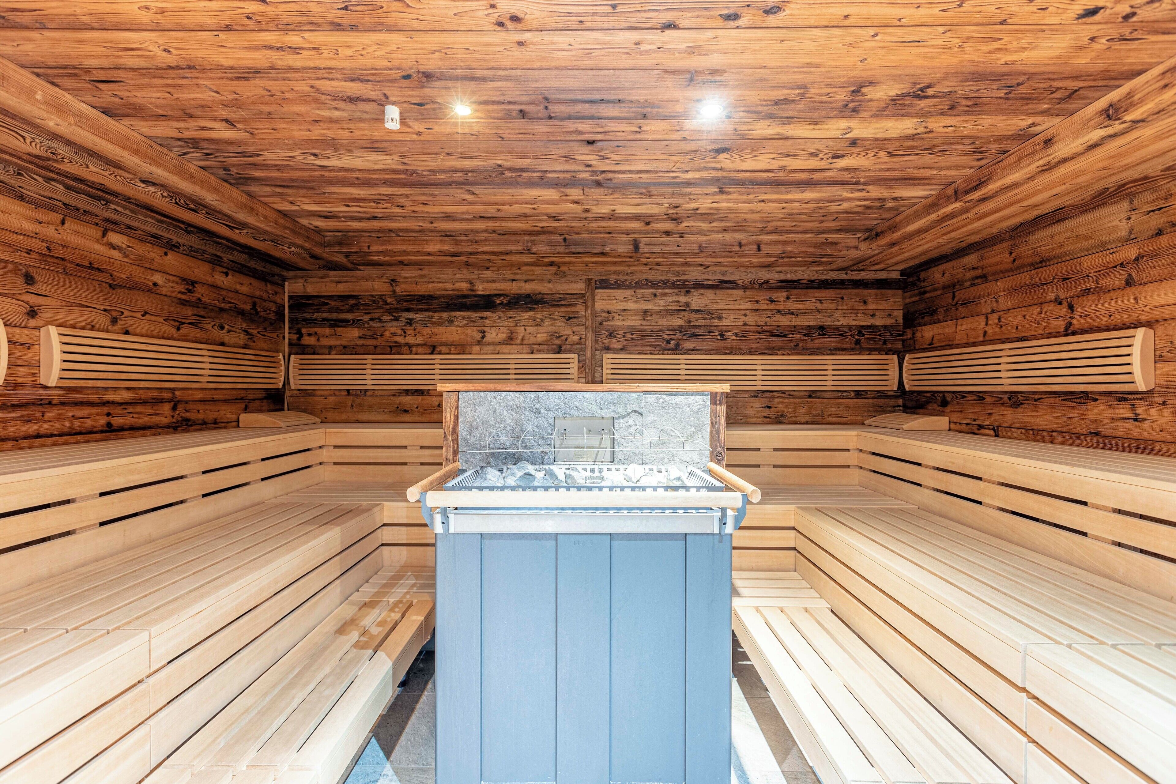 A sauna room with wooden walls and benches, a central heating unit, and ventilation panels.