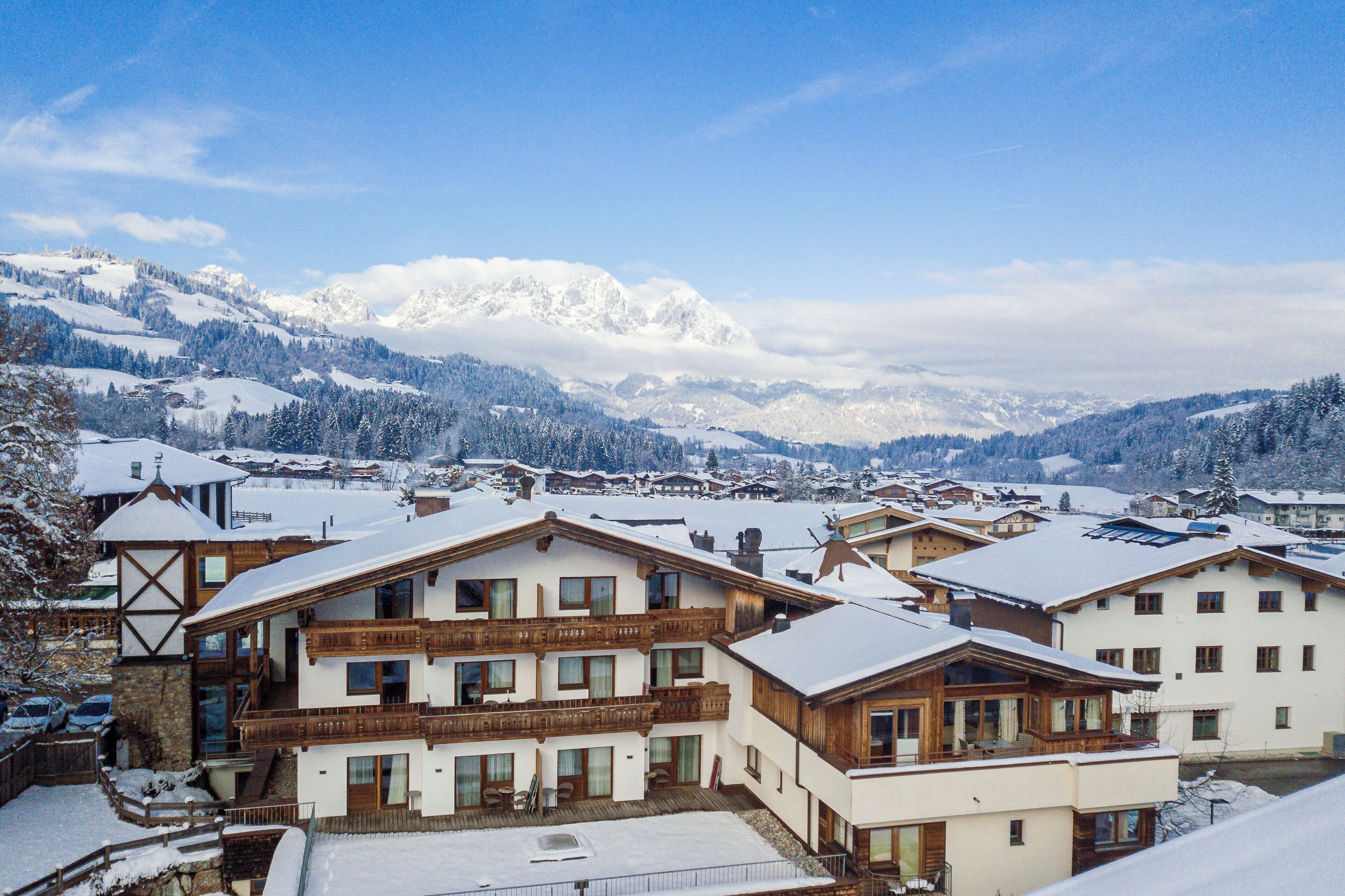 A snow-covered mountain village with traditional wooden buildings and a clear view of the snow-capped peaks in the background.