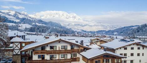 A snow-covered mountain village with traditional wooden buildings and a clear view of the snow-capped peaks in the background.