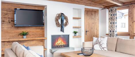 Un salon chaleureux doté d’une cheminée, d’un plafond en bois et d’un téléviseur à écran plat fixé au mur.
