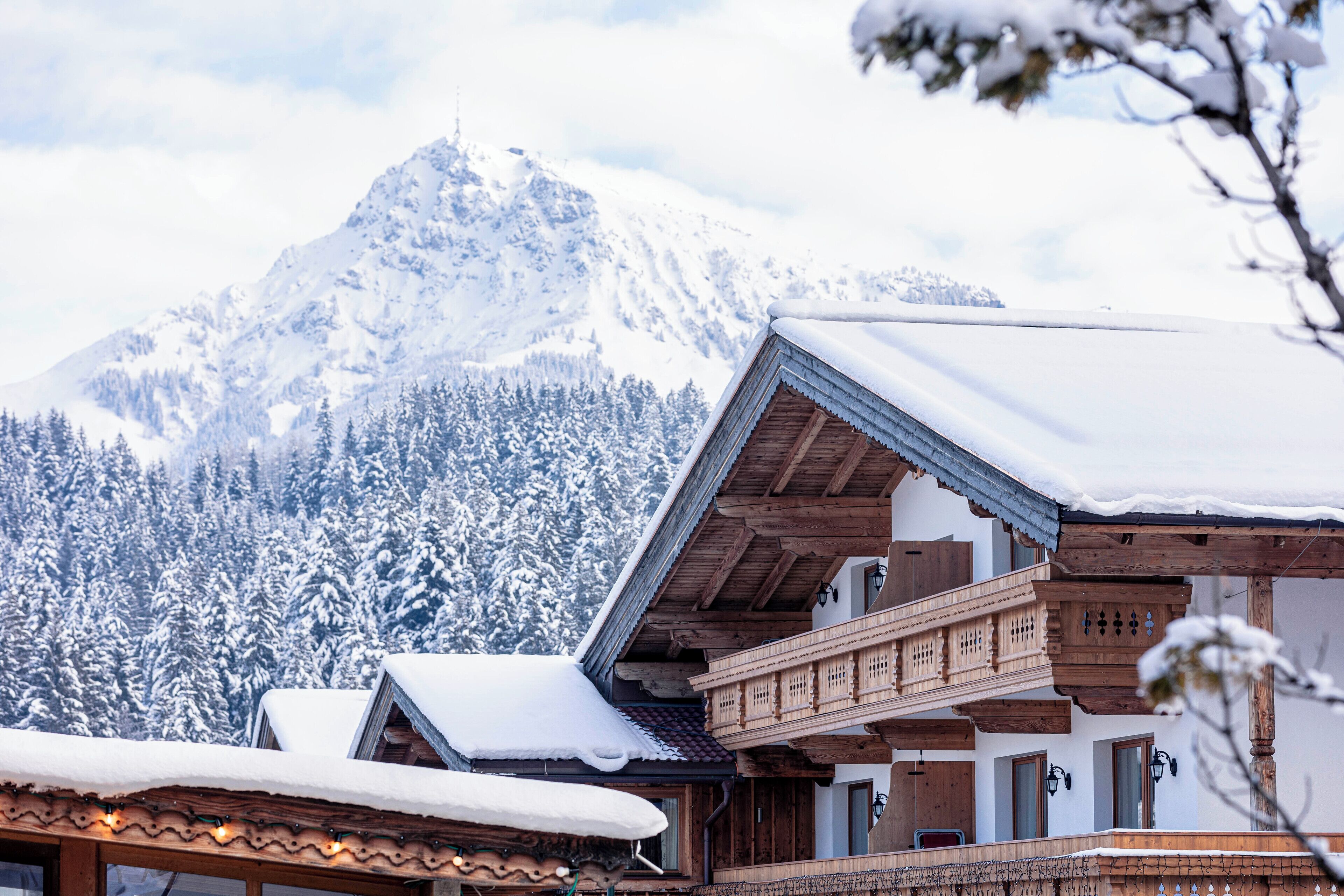 A traditional wooden chalet with a snow-covered roof, set against a backdrop of snow-laden mountains.