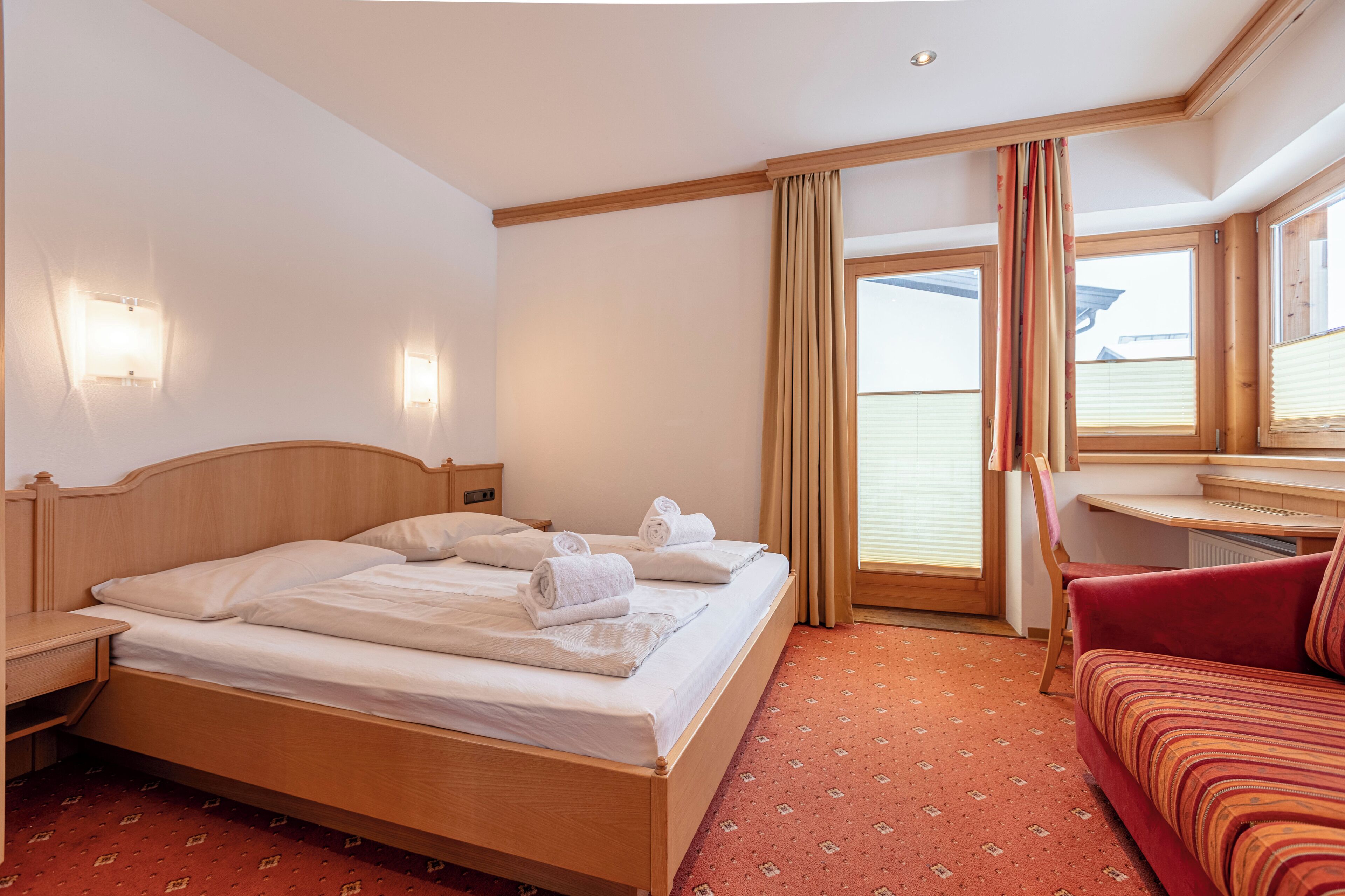A hotel room with a wooden bed, a red sofa, and a window with curtains.