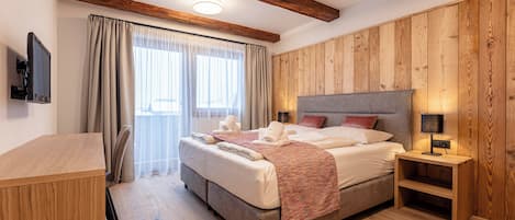 A bedroom with a wooden ceiling, a bed with a grey headboard, a bedside table with a lamp, and a TV on the wall.