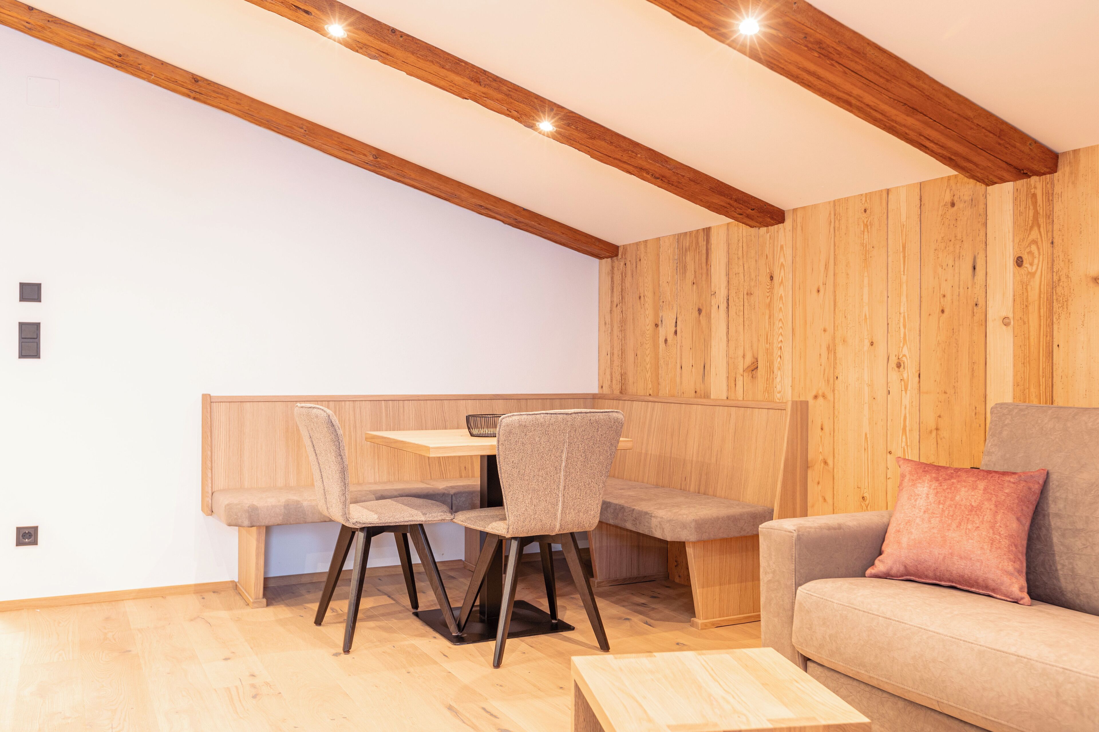 A modern living room with wooden beams, a sofa, and a dining table with chairs.