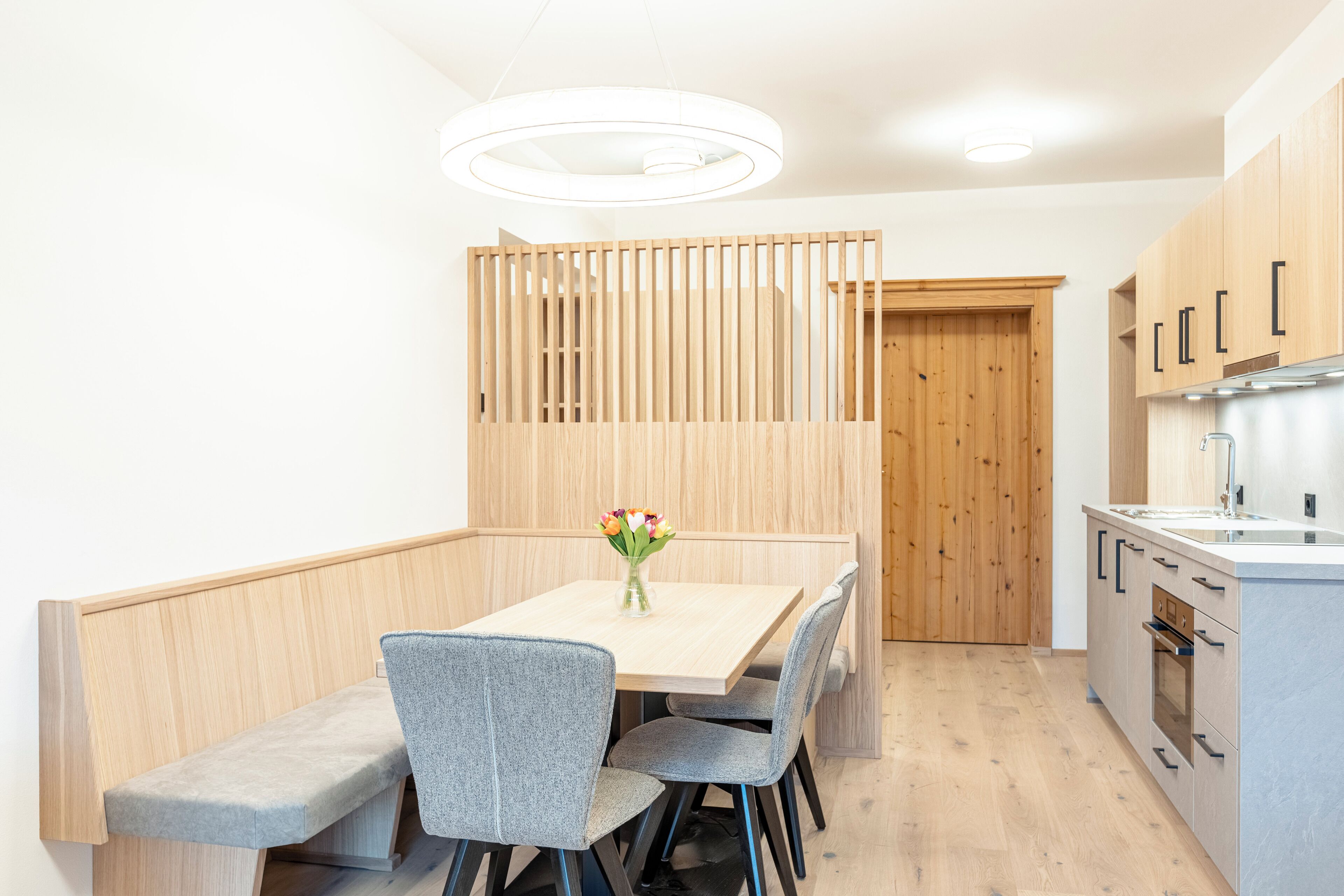 A modern kitchen with wooden cabinets, a built-in oven, and a dining area with a table and chairs.