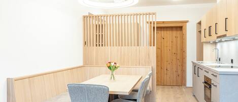A modern kitchen with wooden cabinets, a built-in oven, and a dining area with a table and chairs.
