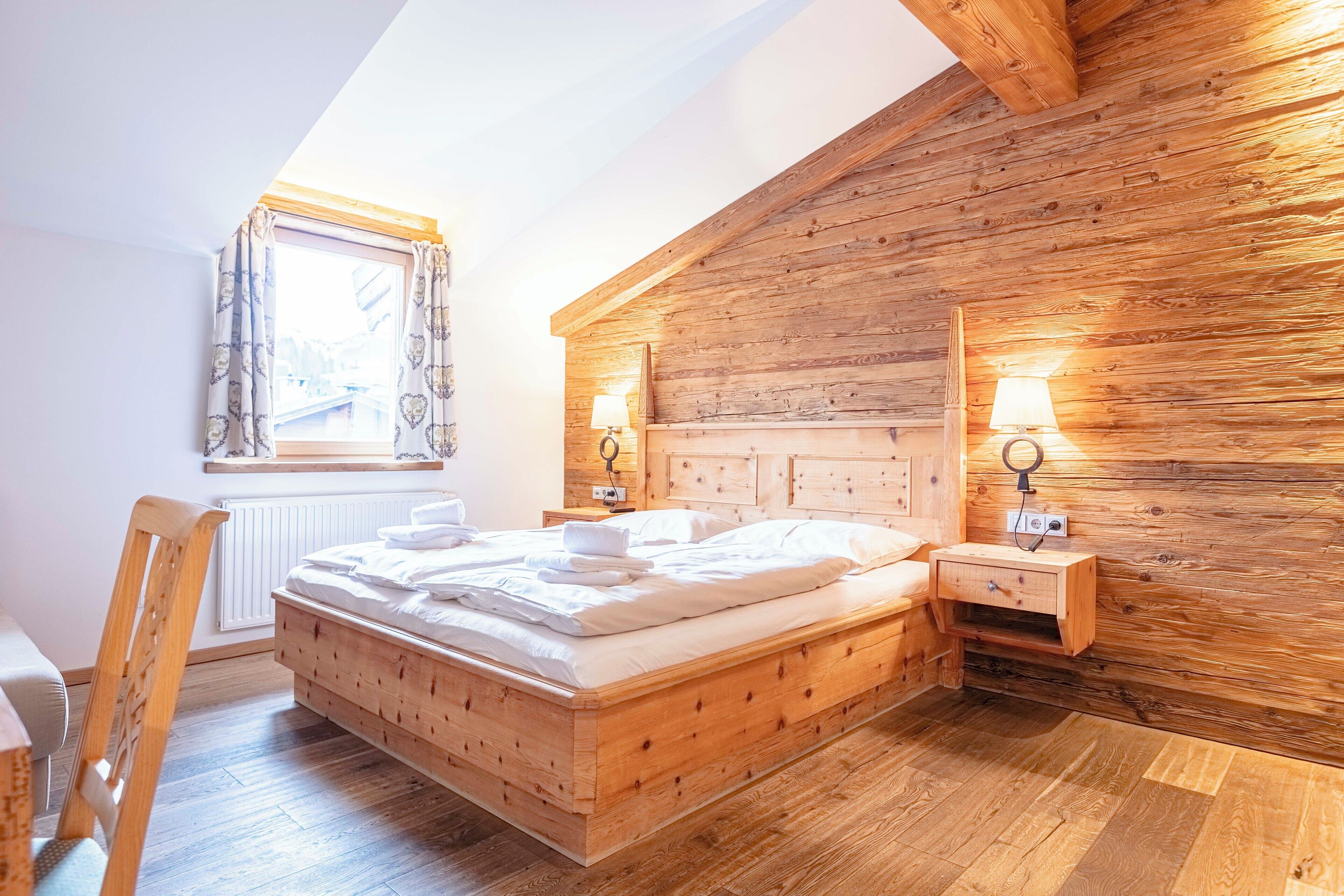 A wooden bedroom with a bed, bedside tables, and a window.