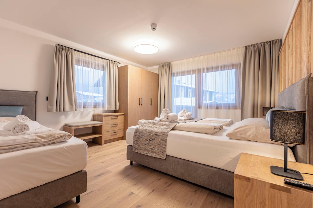 A hotel room with two beds, a desk, a wardrobe, and a TV.